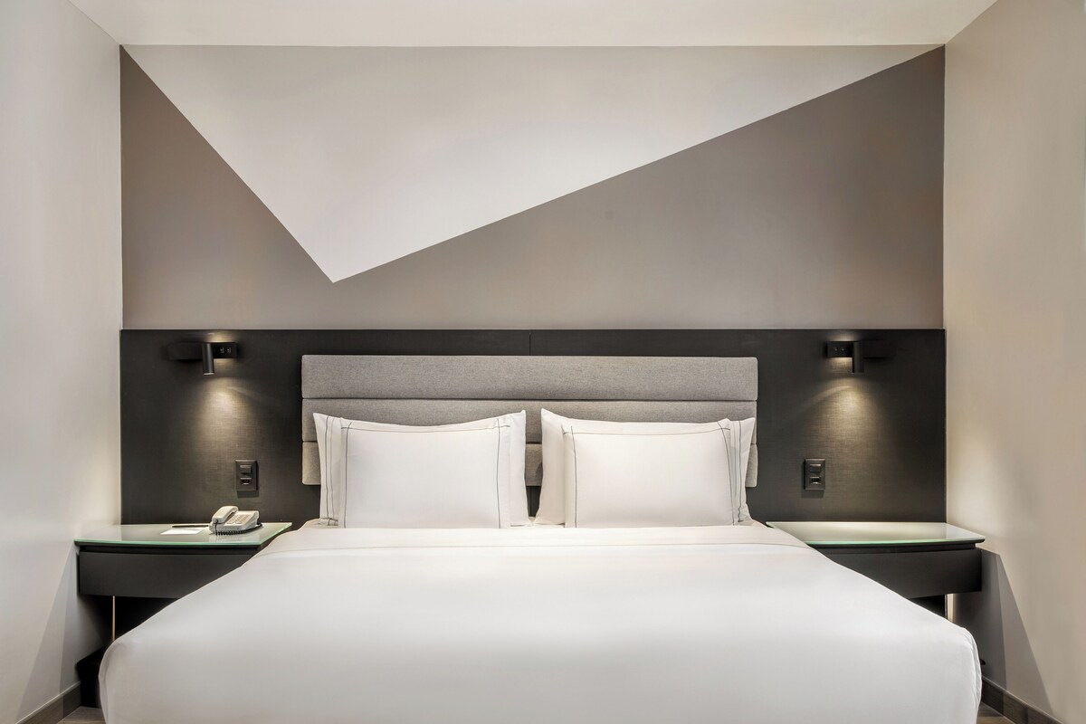 Una habitación de hotel moderna con una cama grande, dos mesitas de noche y un diseño de techo geométrico original.