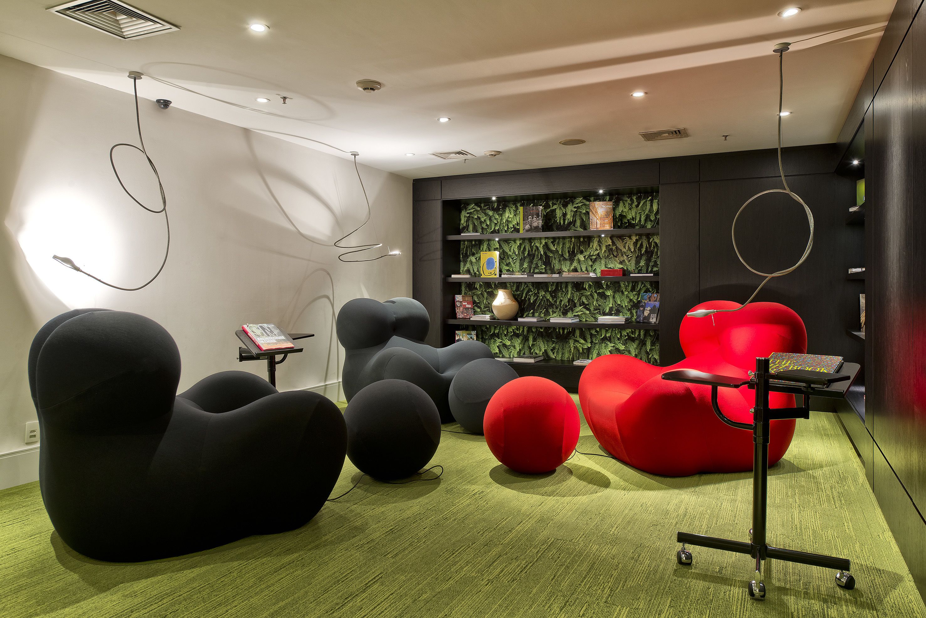Un intérieur moderne avec des sièges noirs et rouges originaux, une moquette verte et une bibliothèque agrémentée de plantes vertes.