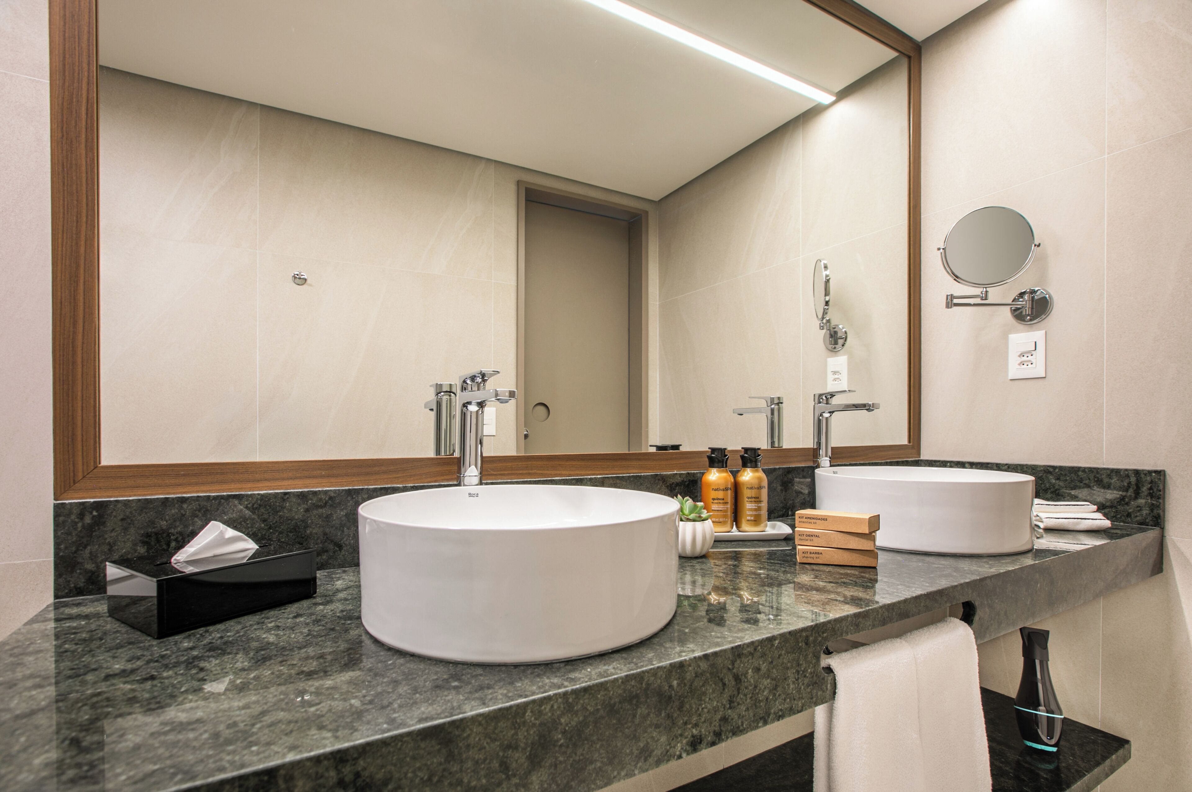 Un baño moderno con dos lavamanos, un espejo grande y artículos de aseo en la encimera.