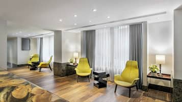 A modern hotel room with wooden flooring, yellow armchairs, a glass coffee table, and a large mirror.