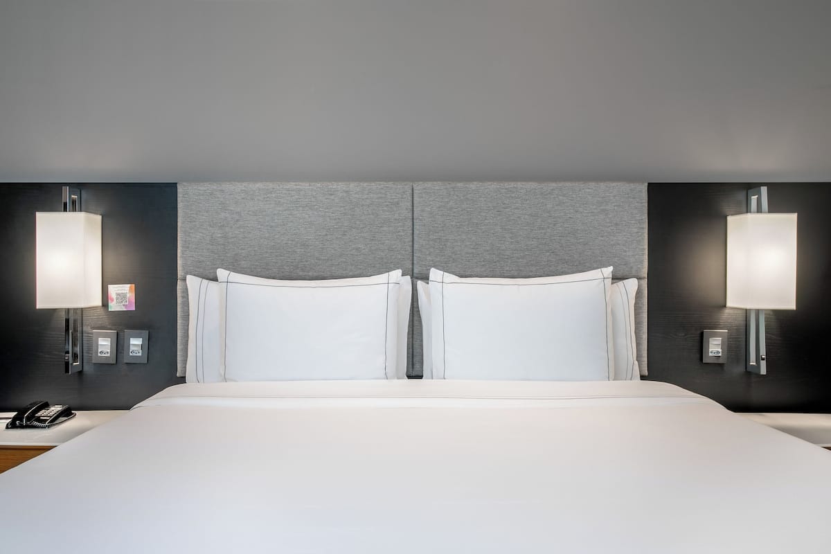 Habitación de hotel con una cama grande, dos lámparas de noche, un teléfono y un panel de control en la pared.