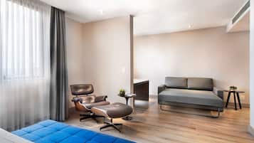 A modern living room with a sofa, a leather armchair, a blue ottoman, and a small table with a plant.