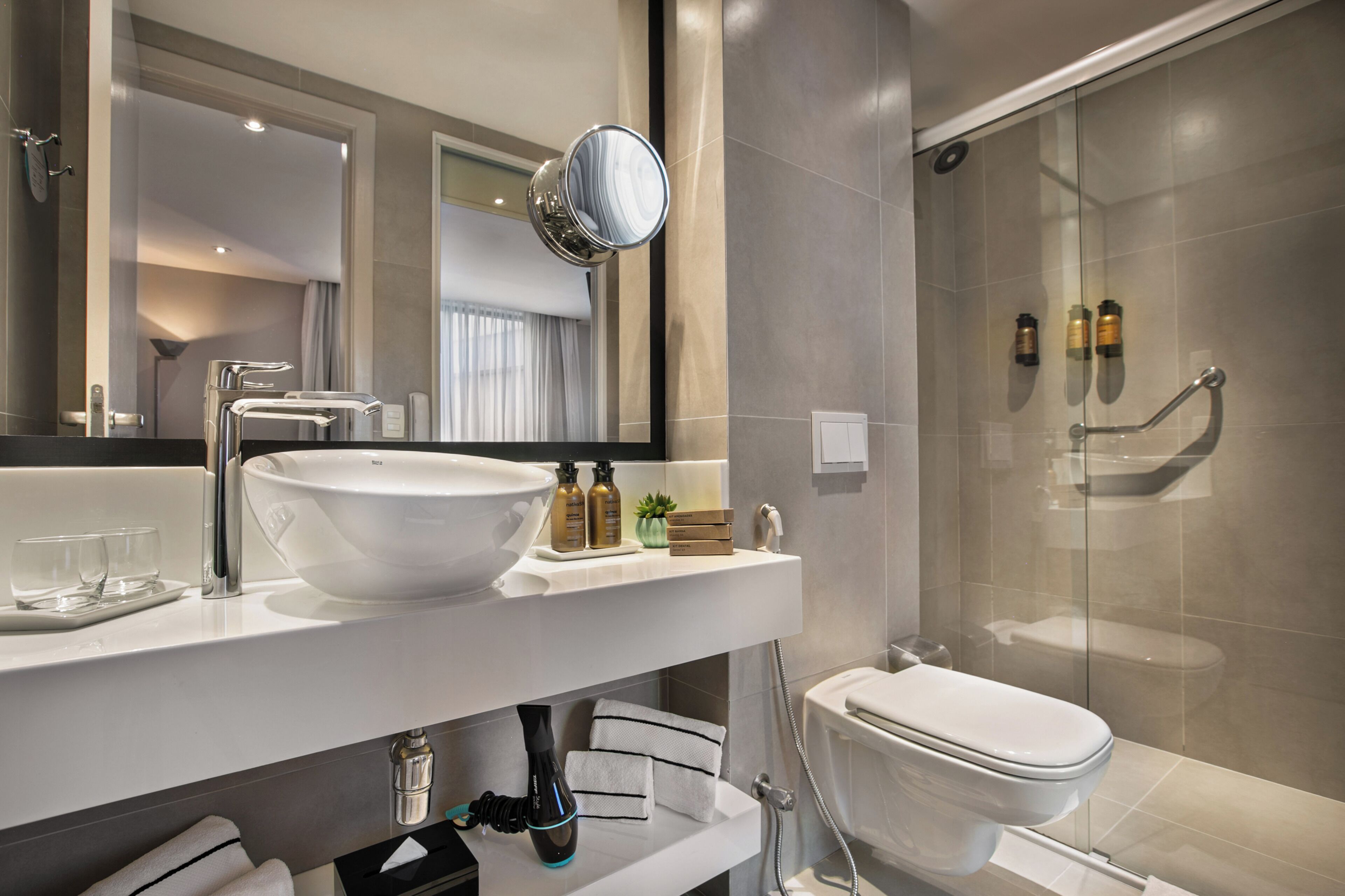 Un baño moderno con un espejo grande, un lavamanos blanco y una cabina de ducha de vidrio.