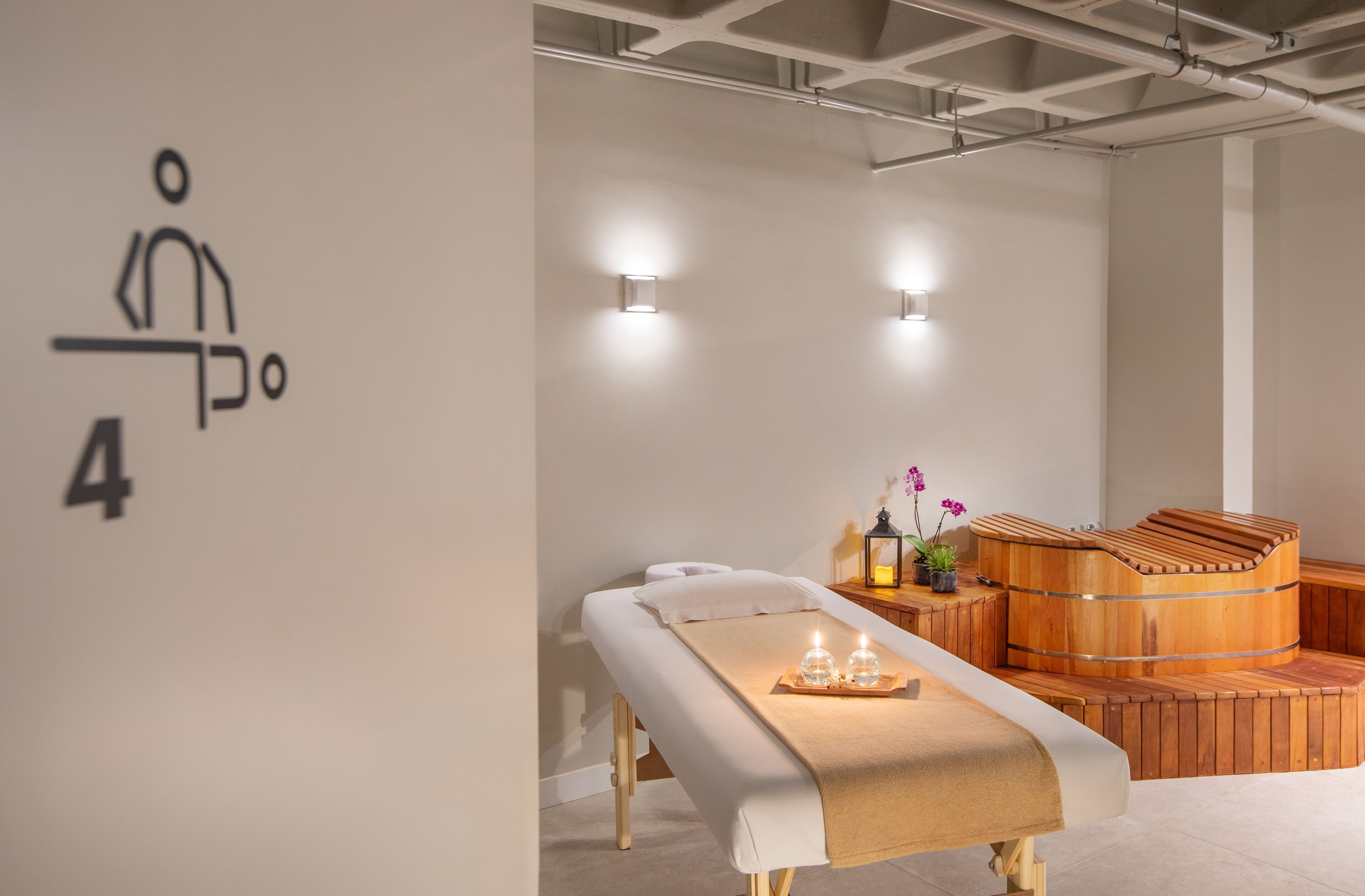 A spa room with a massage table, a wooden sauna, and wall-mounted lights.