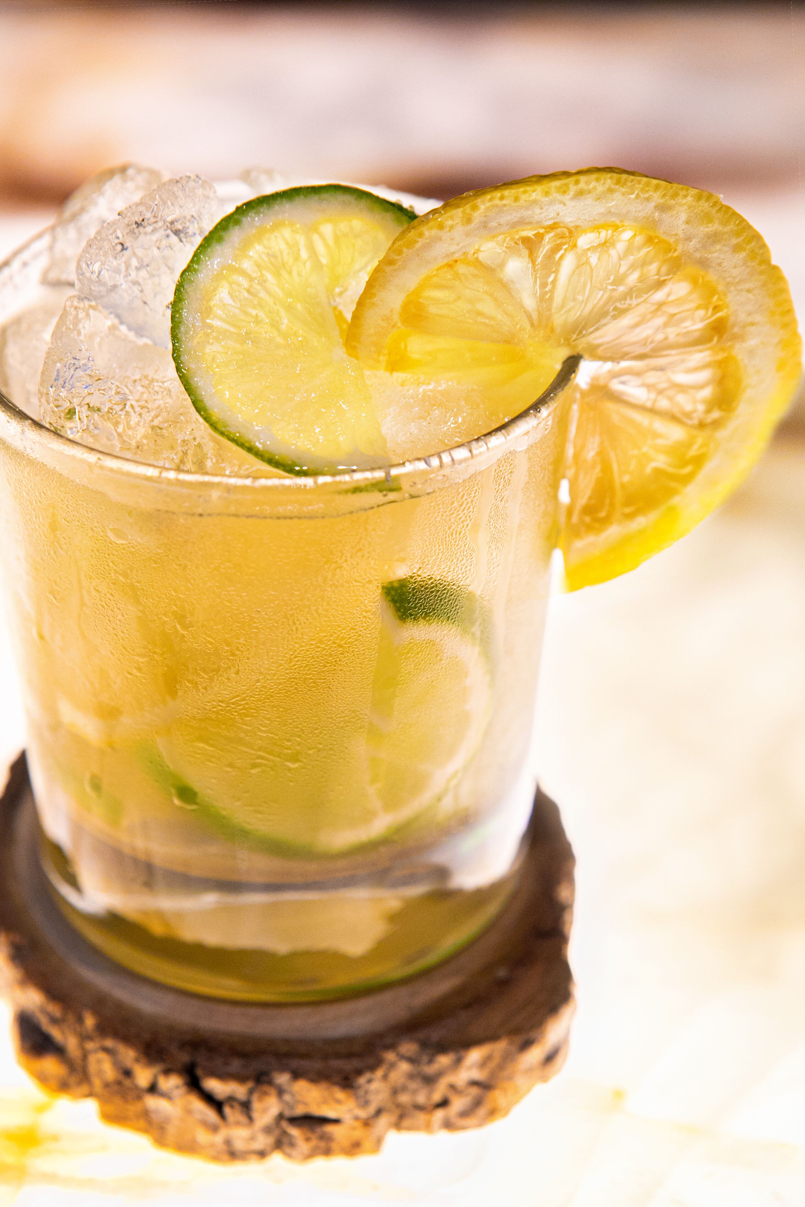 A glass of iced beverage with lime slices, served on a coaster.