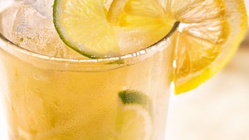 A glass of iced beverage with lime slices, served on a coaster.