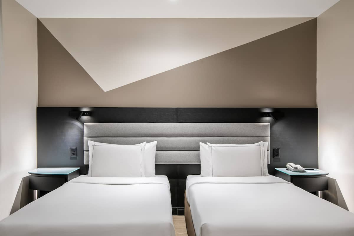 Una habitación de hotel moderna con dos camas individuales, un escritorio y una mesita de noche con teléfono.