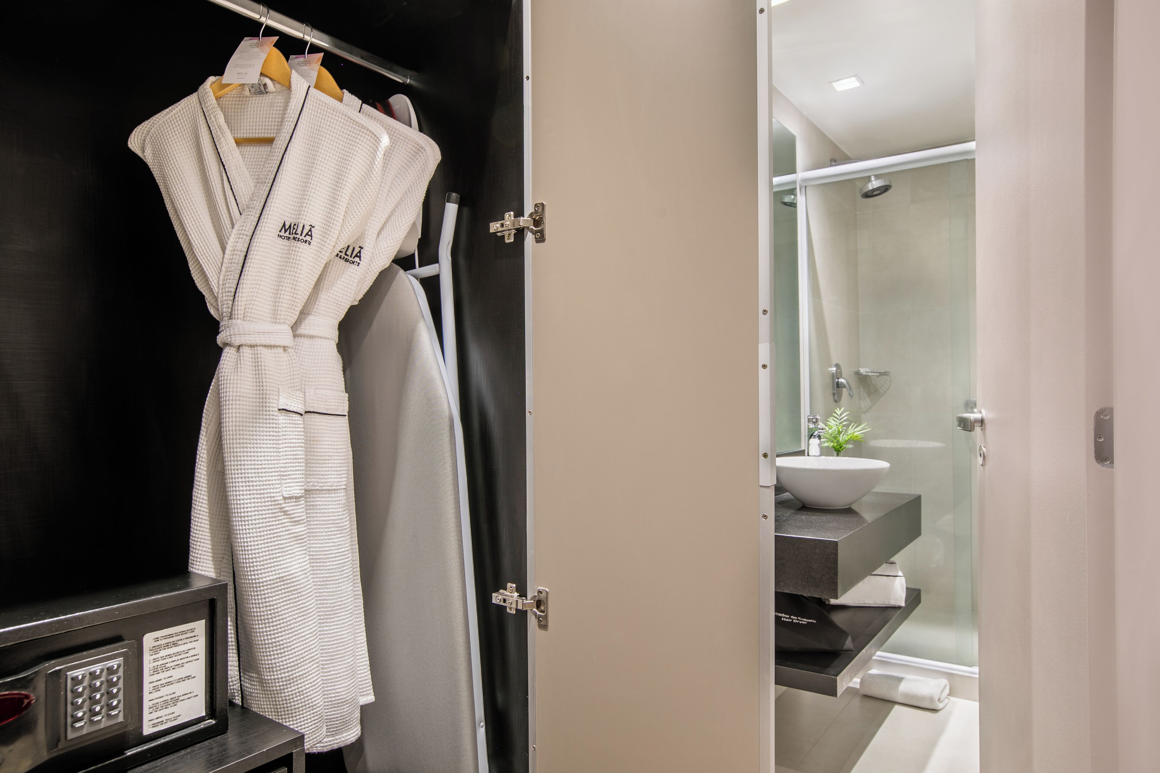 A bathroom with a glass shower enclosure, a sink, and a towel rack with robes.