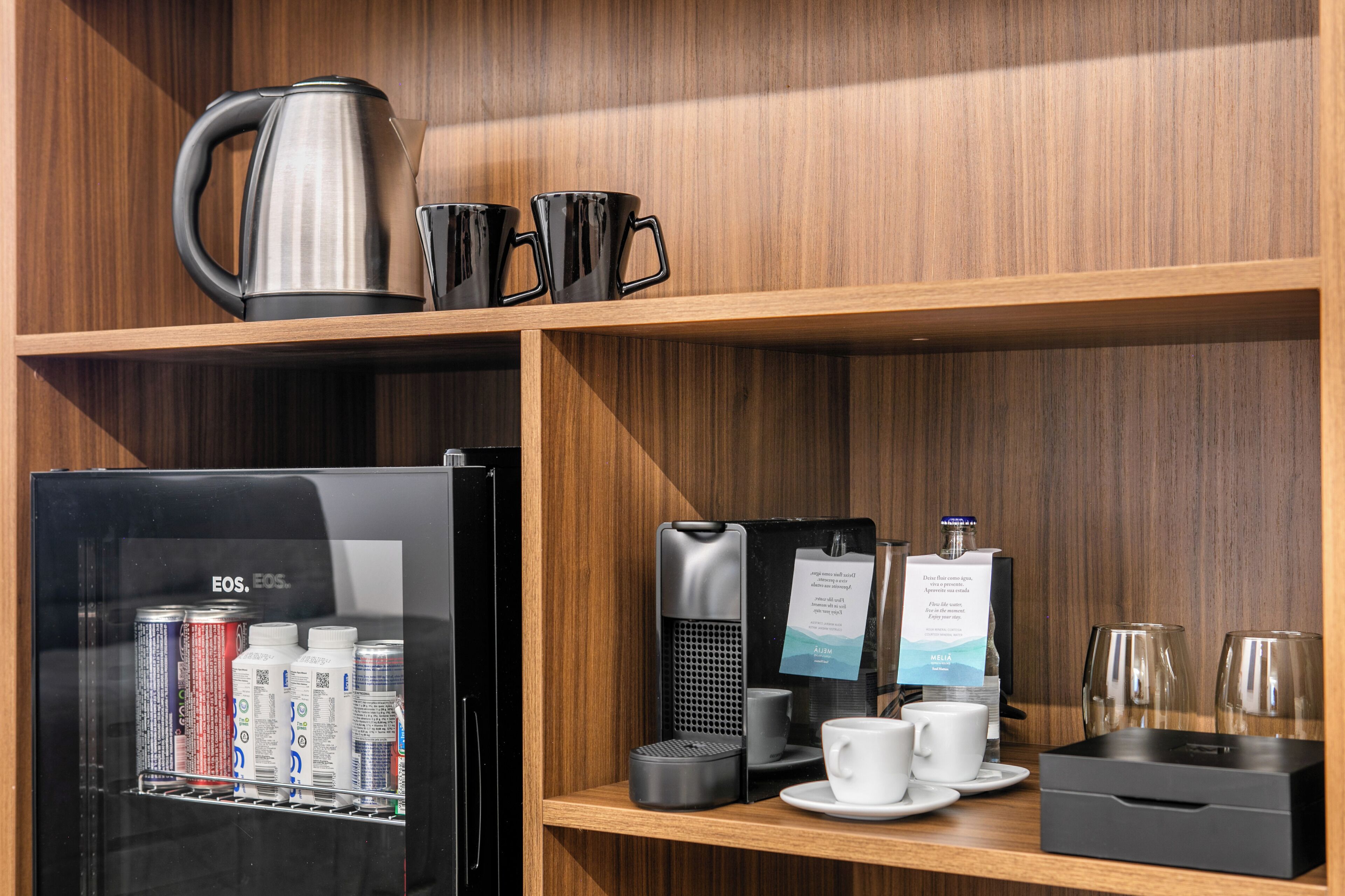 A coffee station with a coffee maker, cups, and a refrigerator stocked with beverages.
