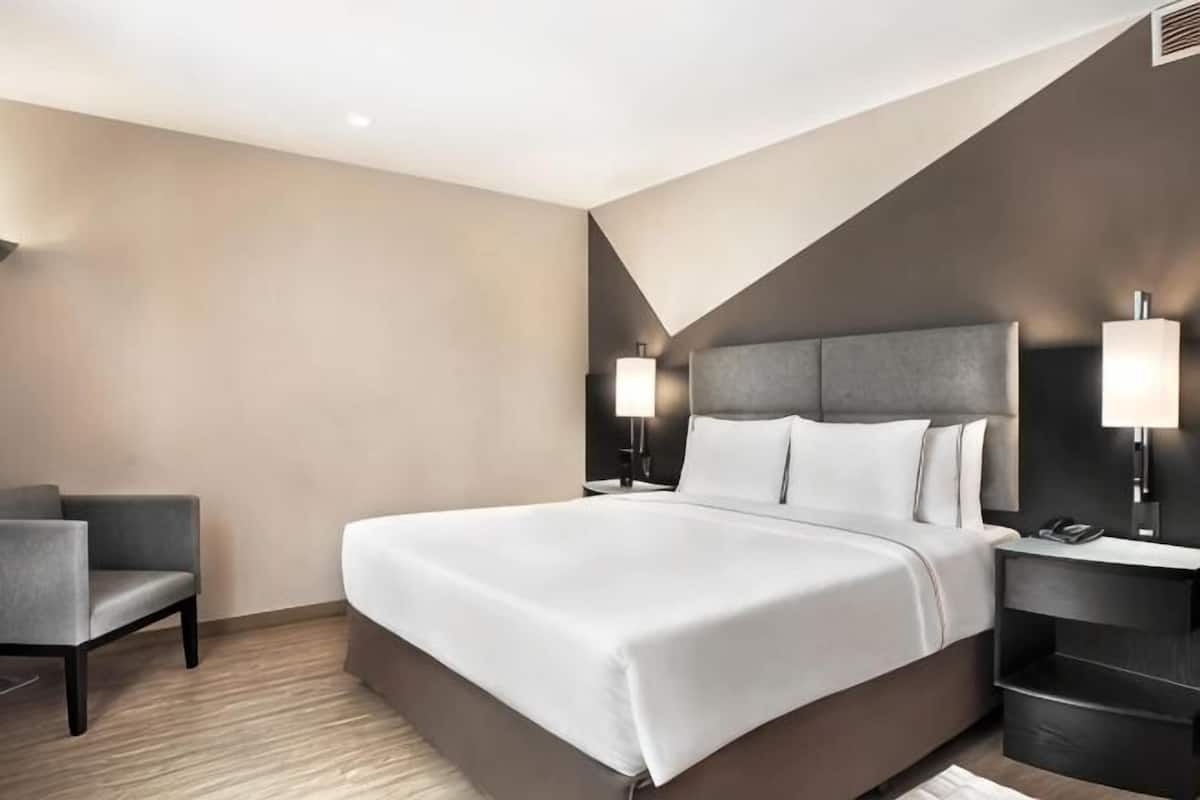 A modern hotel room with a large bed, bedside tables, a desk, and a chair.