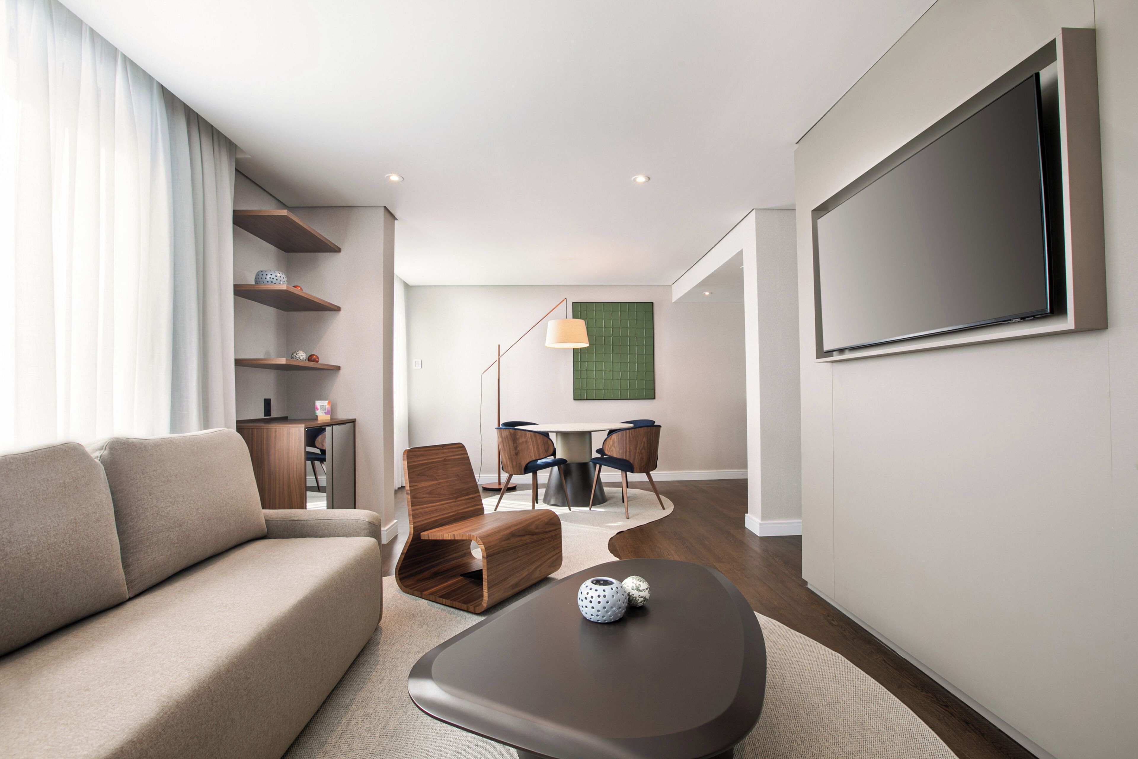 Ett modernt hotellrum med en soffa, ett soffbord, en TV, en matplats och ett skrivbord.