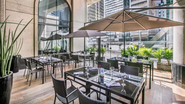 Un espace extérieur aménagé pour les repas, avec des tables et des chaises, de grands parasols et des plantes en pot.