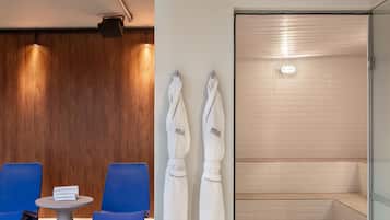 Uma sauna a vapor com paredes revestidas de azulejos brancos e uma parede de painéis de madeira ao fundo. Há duas toalhas brancas penduradas em ganchos e uma pequena mesa com uma pilha de livros.