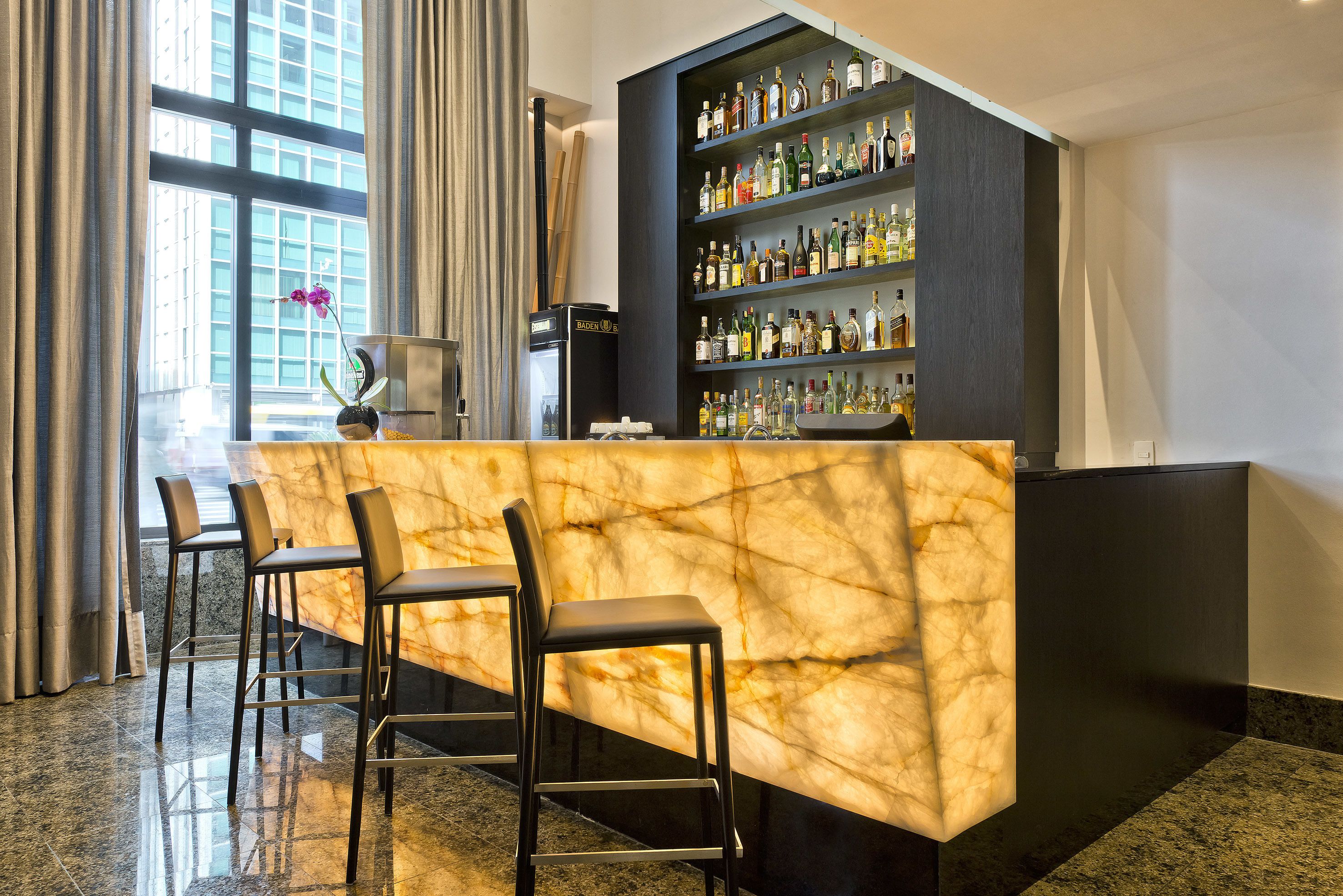 A bar area with a marble counter, bar stools, and a liquor display.