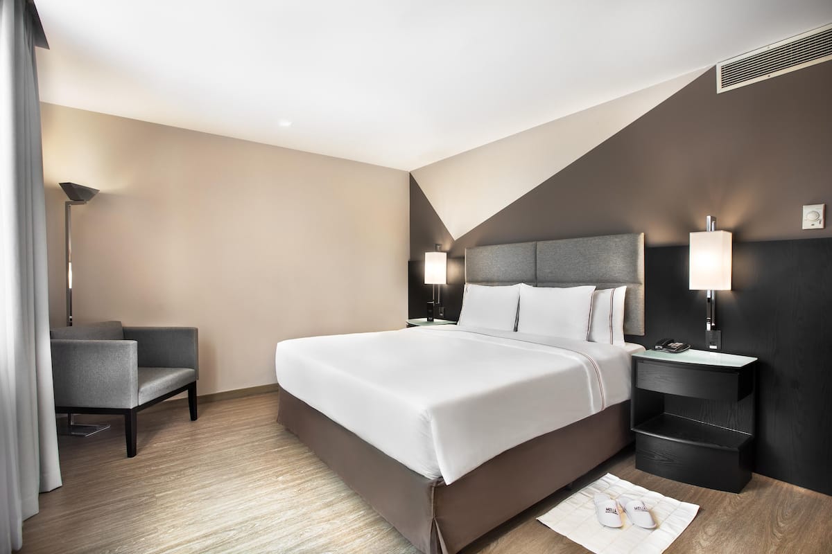 Una habitación de hotel moderna con una cama grande, mesitas de noche, una silla y un escritorio.