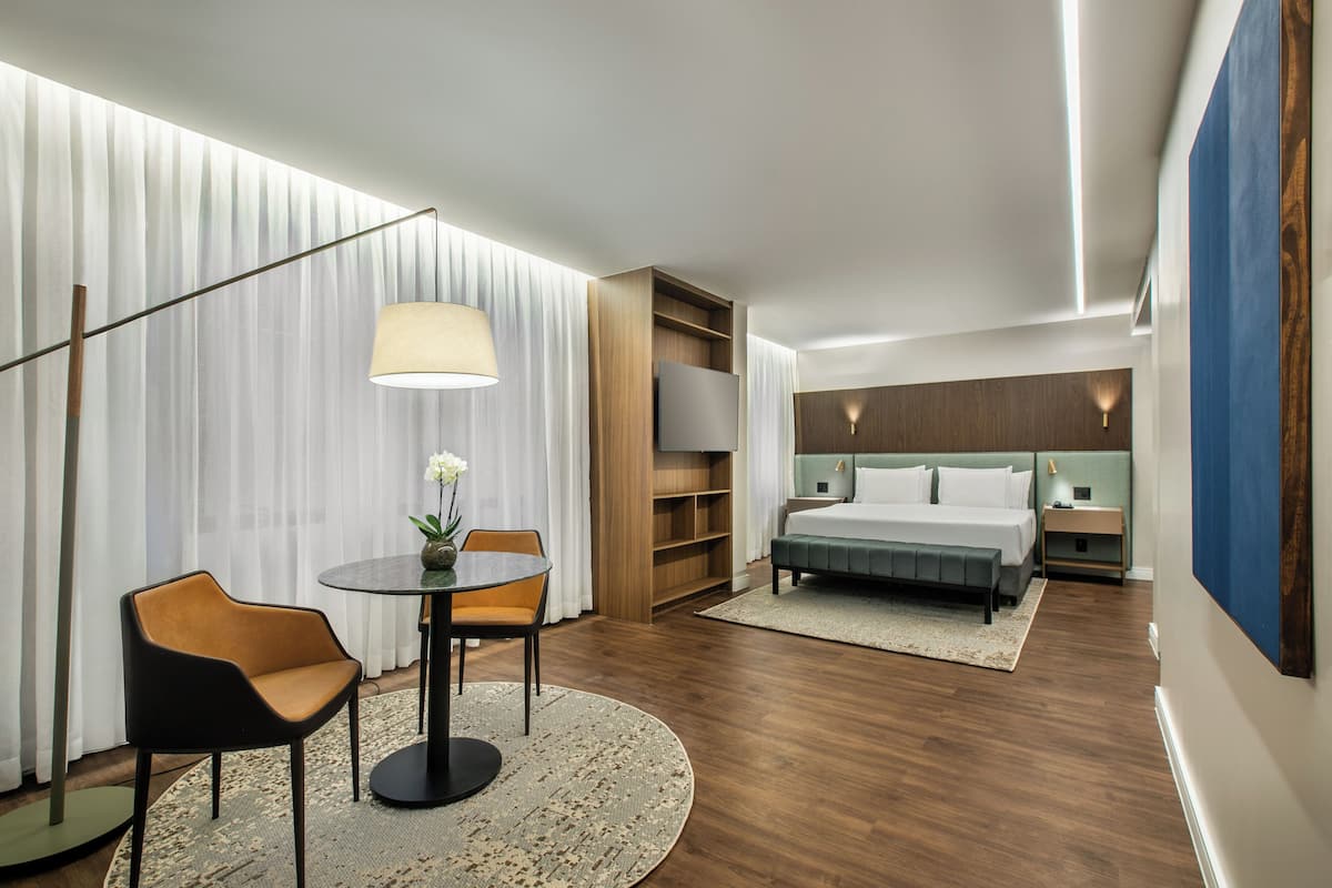 Una habitación de hotel moderna con una cama, un escritorio con lámpara, una silla y un televisor.