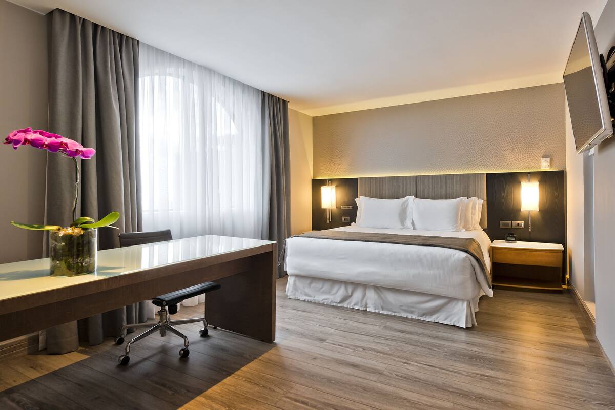 Una habitación de hotel con una cama, mesitas de noche, un escritorio y una silla.
