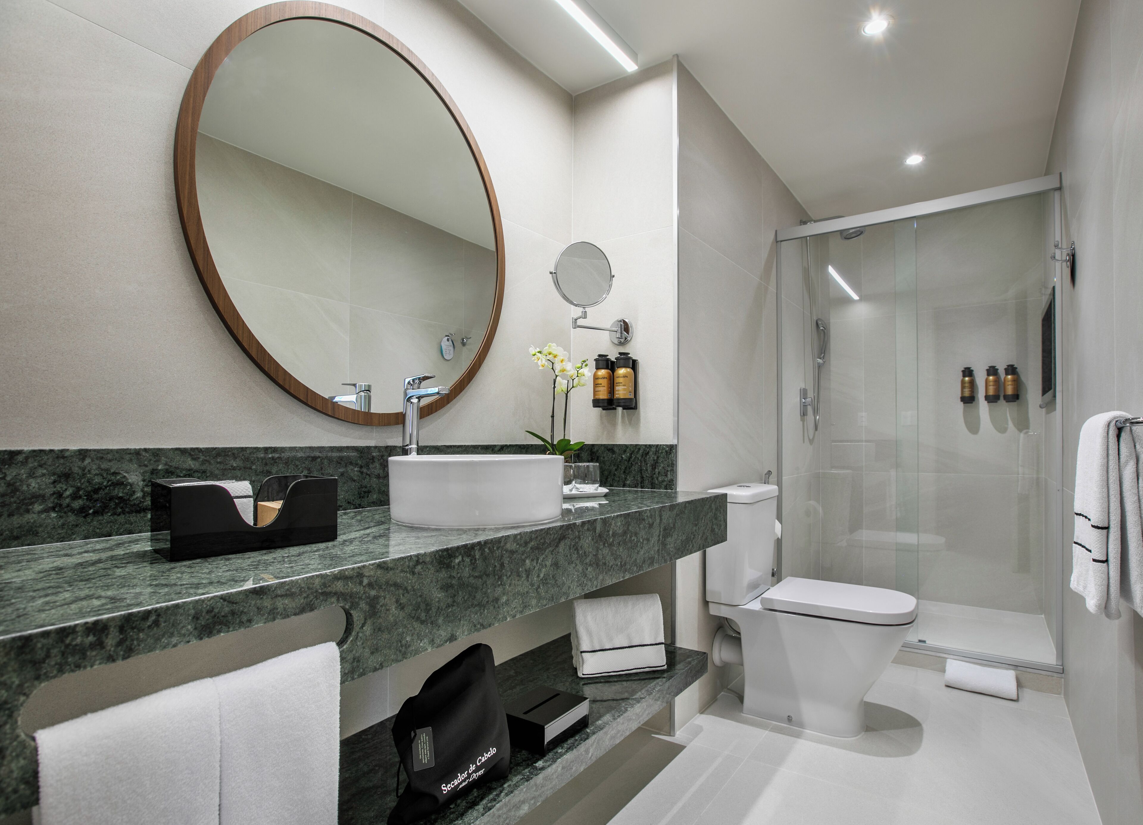 A modern bathroom with a marble countertop, a large mirror, a toilet, and a glass-enclosed shower.