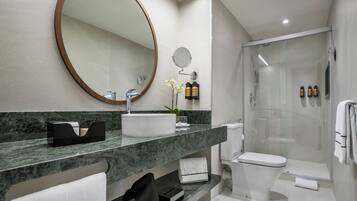 A modern bathroom with a marble countertop, a large mirror, a toilet, and a glass-enclosed shower.