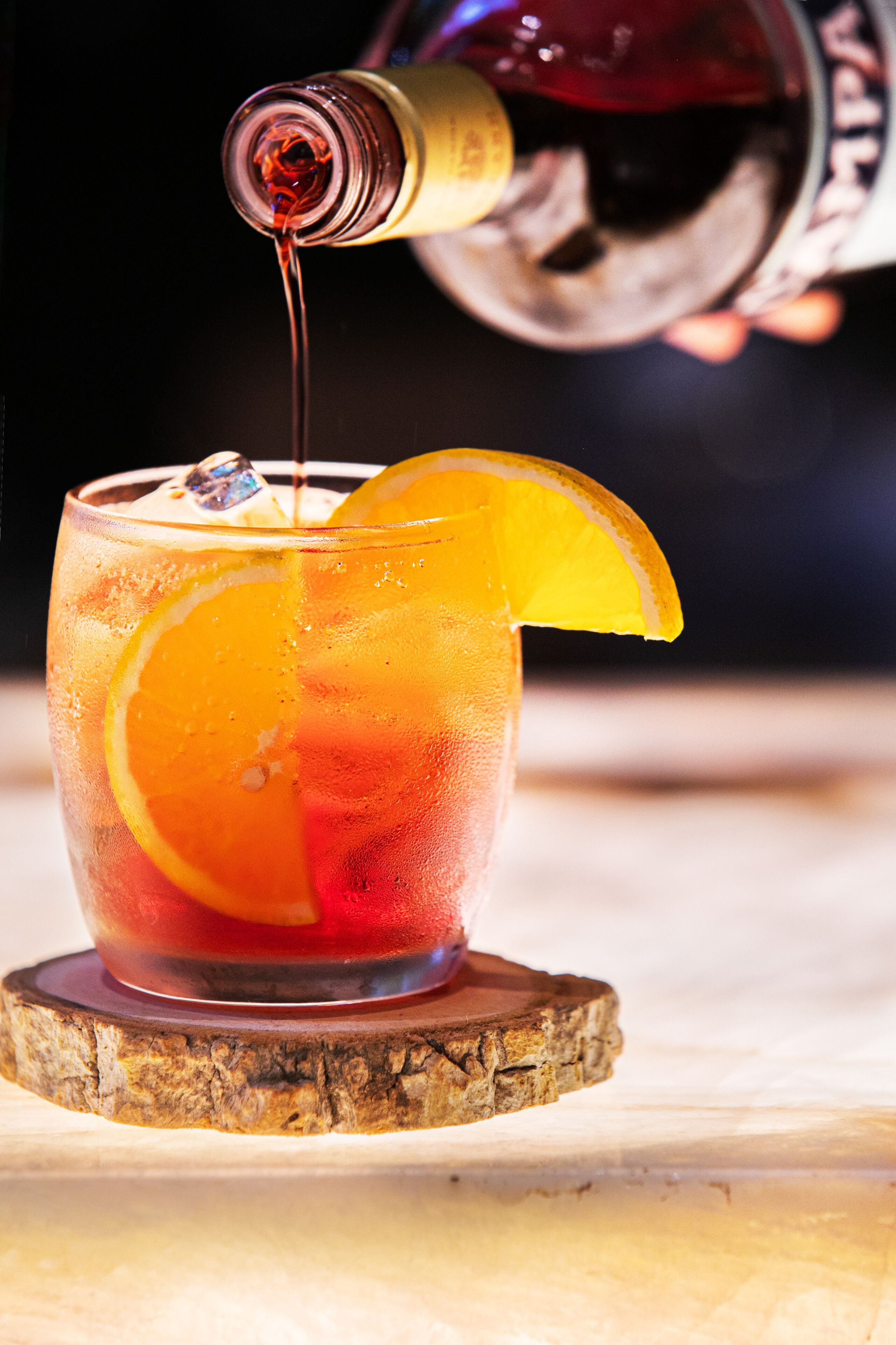 Um copo de cocktail com uma fatia de laranja e cubos de gelo, apoiado num apoio de madeira.