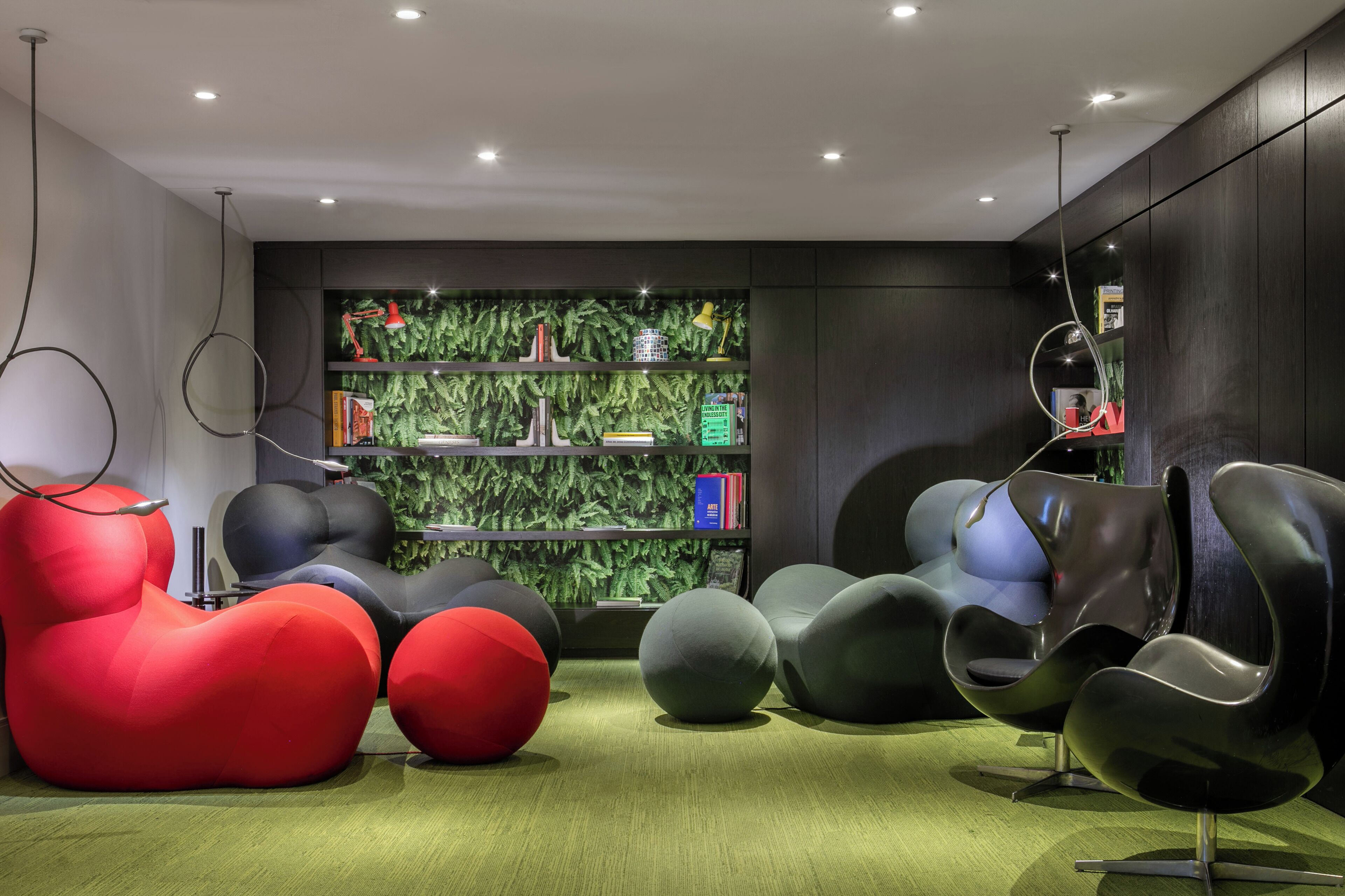 Un interior moderno con asientos únicos, una pared verde con plantas y una estantería.