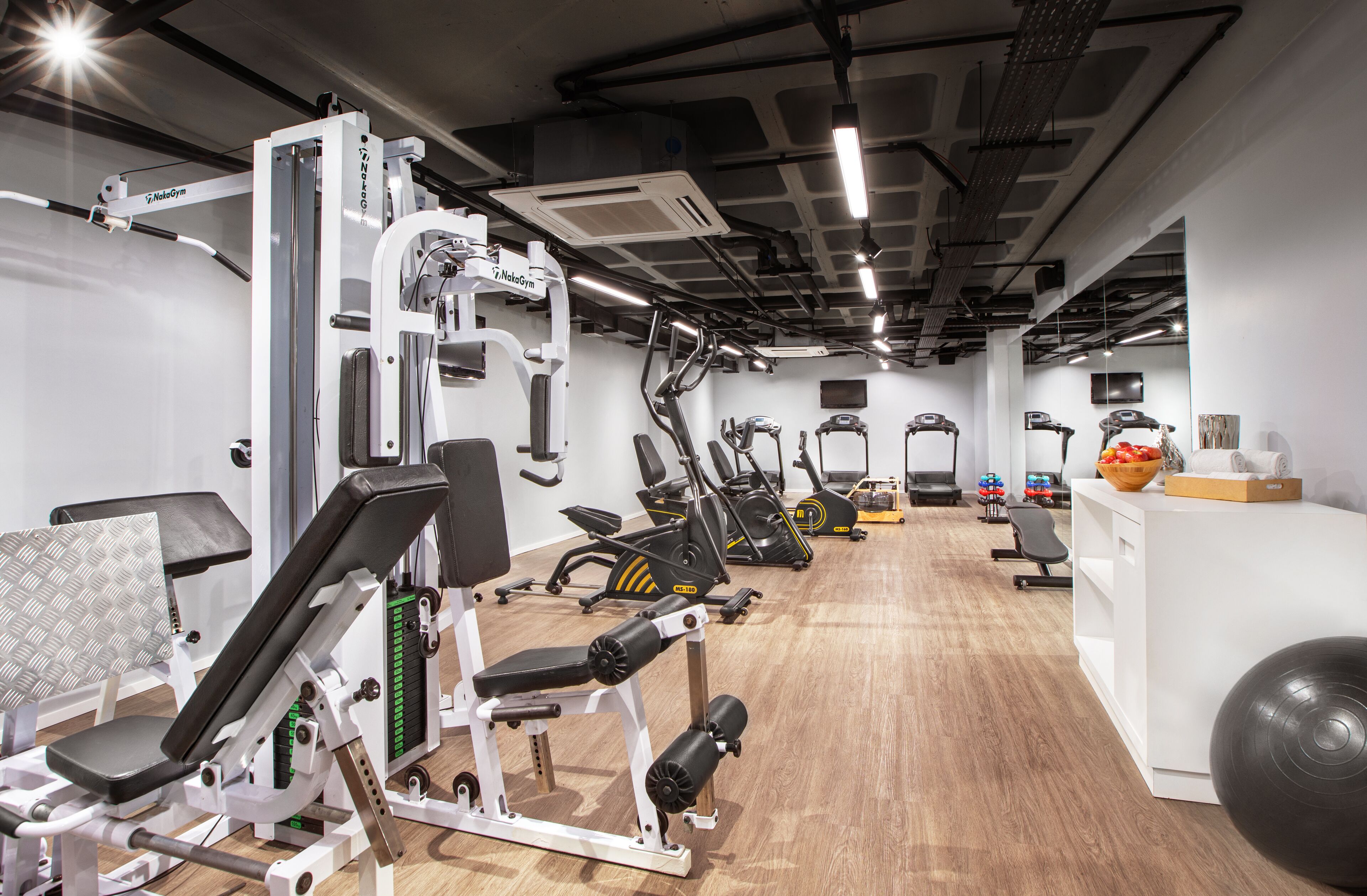 Un gimnasio con diversos equipos de ejercicio, entre ellos cintas de correr, máquinas de pesas y una máquina de remo.