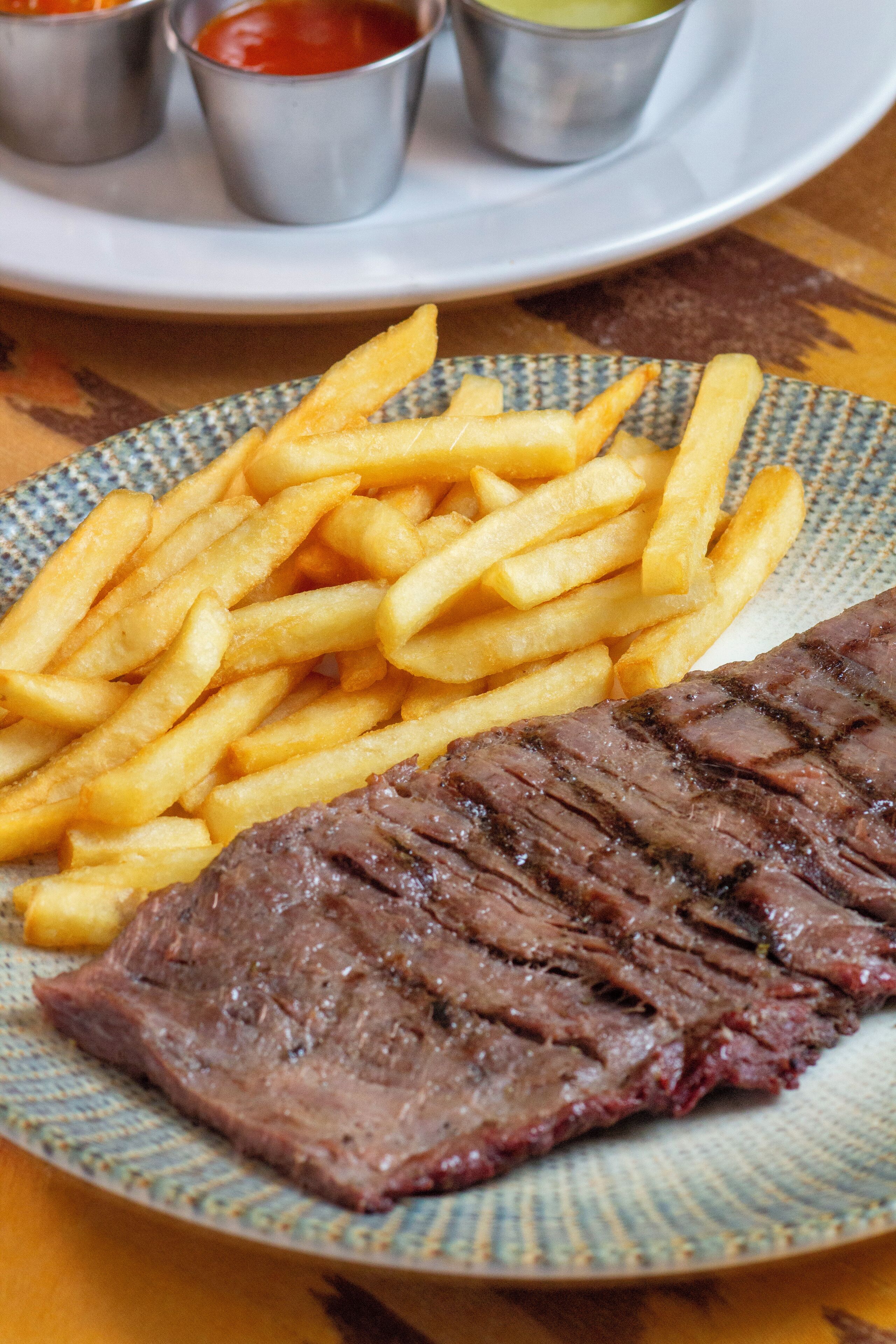 A plate with steak and fries, accompanied by small metal cups of sauces.