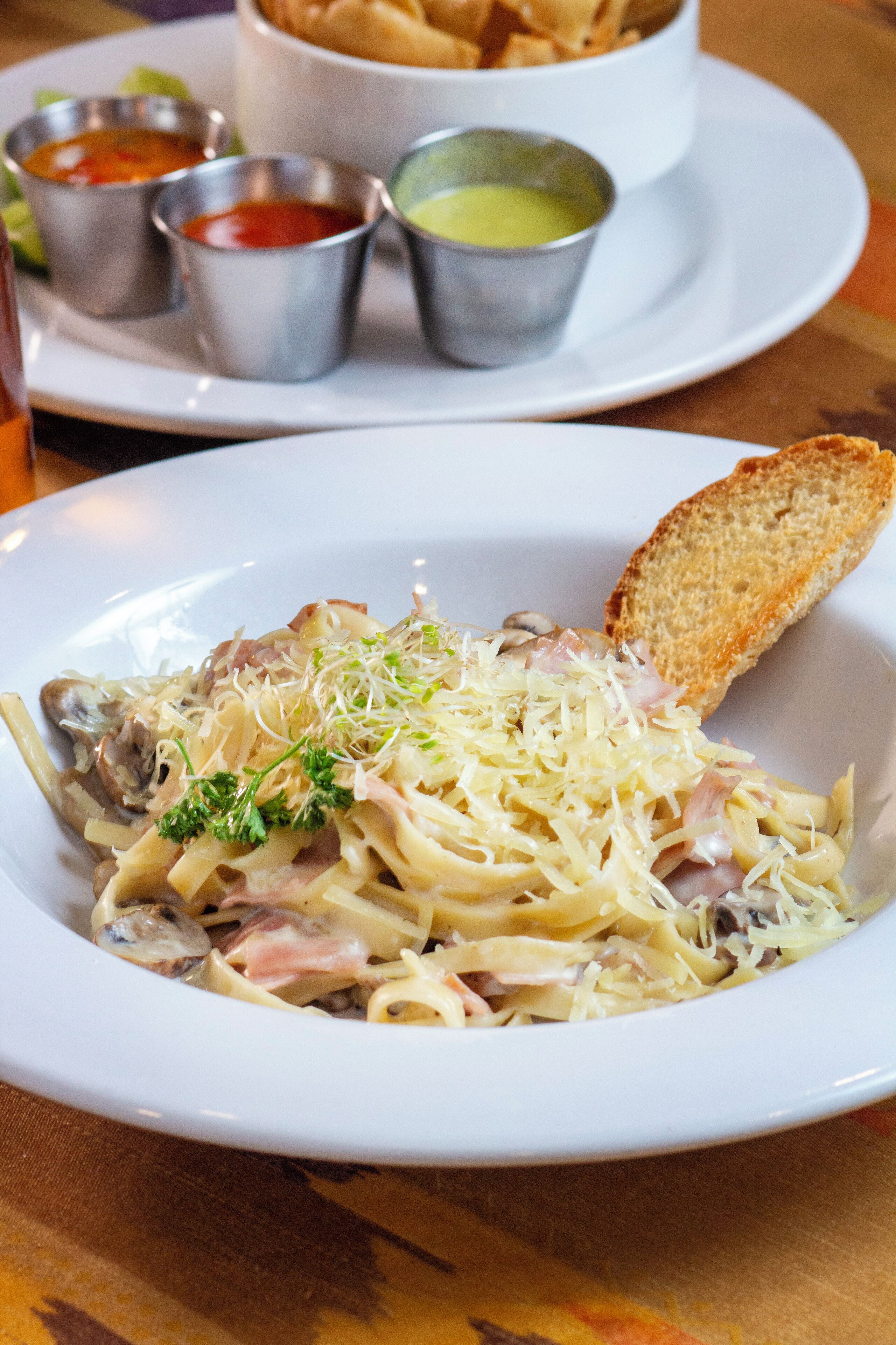 A plate of pasta with a slice of bread and three small containers of sauces.