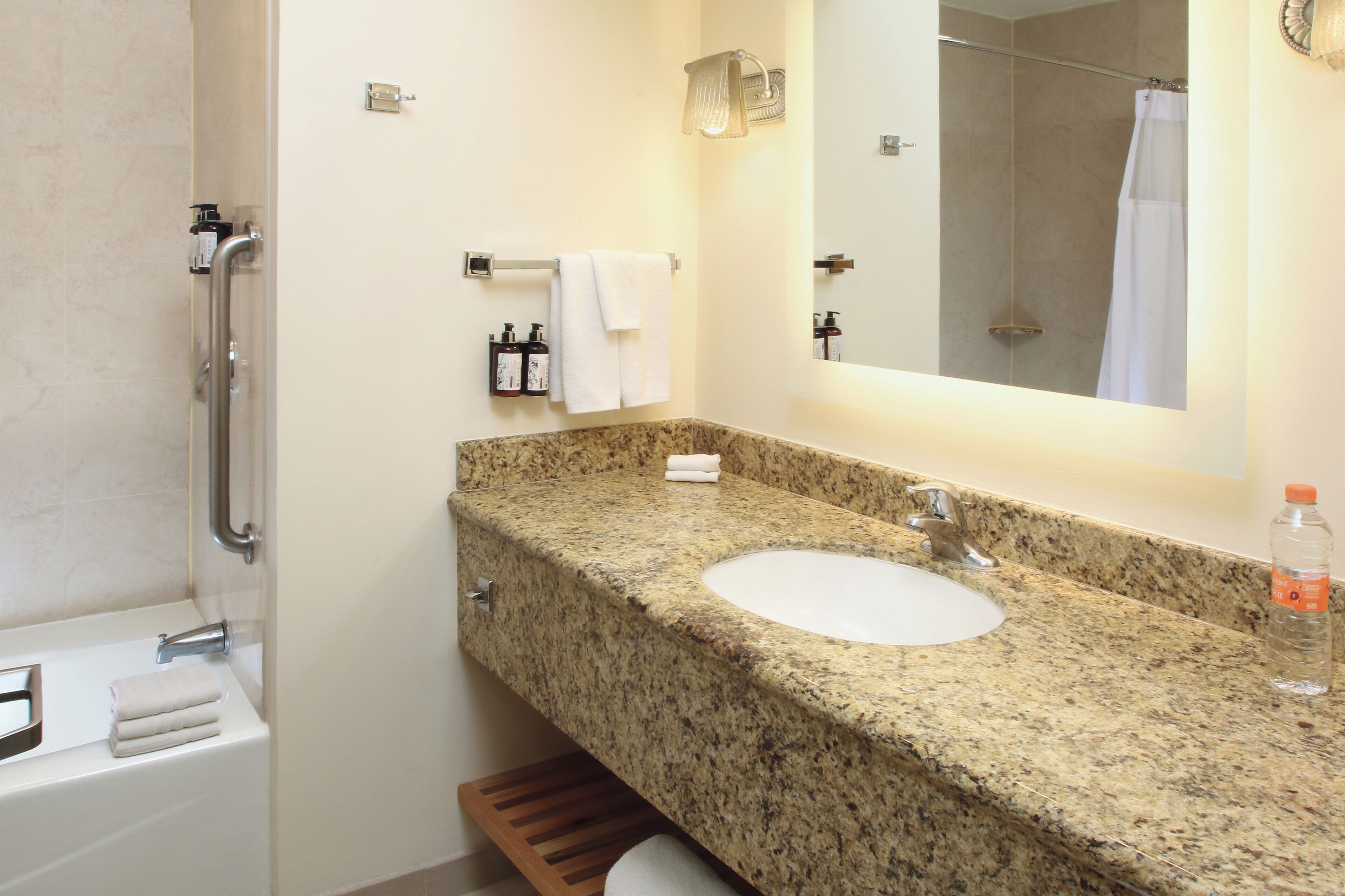 A bathroom with a granite countertop sink, a mirror, a shower, and a towel rack.