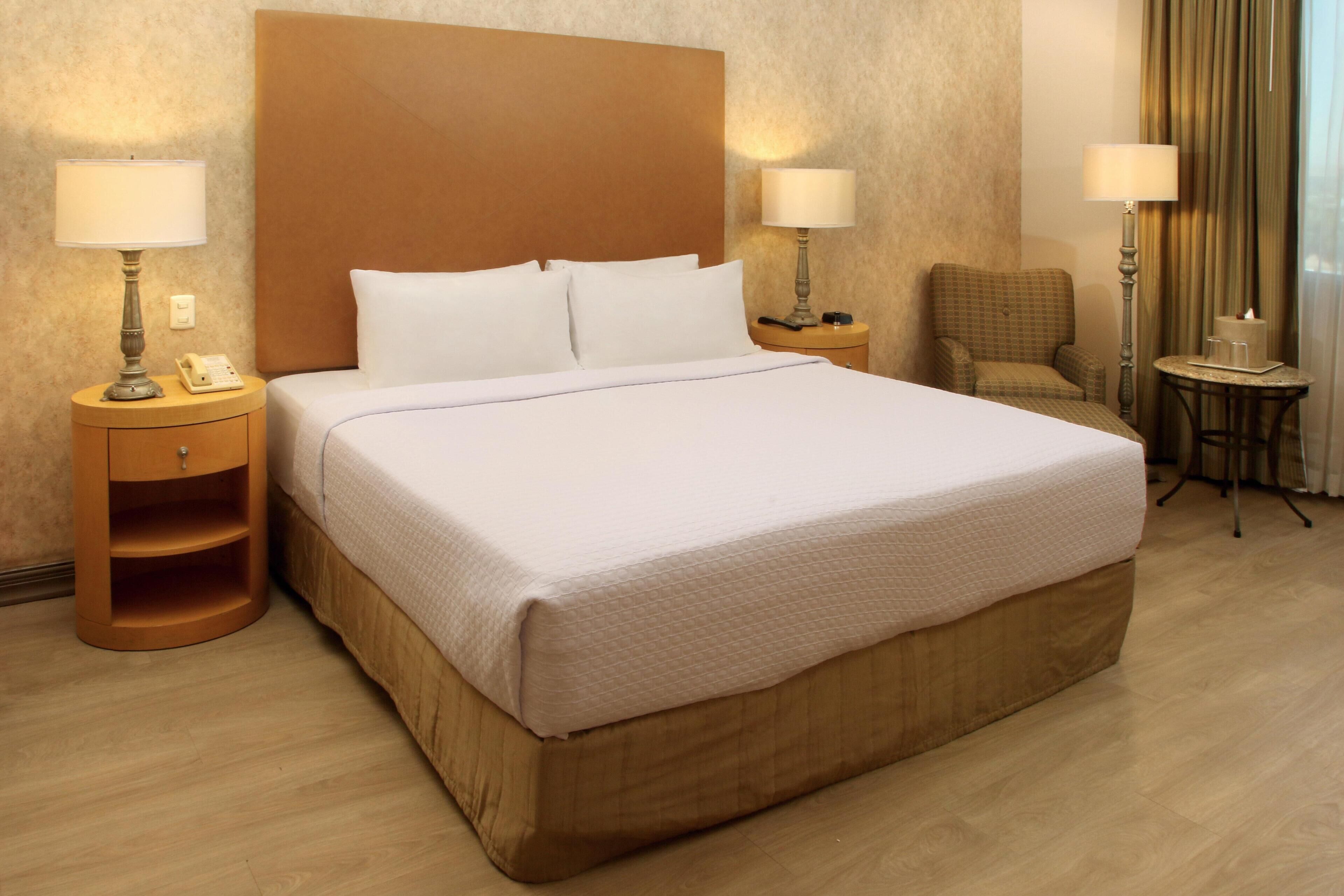A hotel room with a large bed, two bedside tables with lamps, a chair, and a small table with a candle.