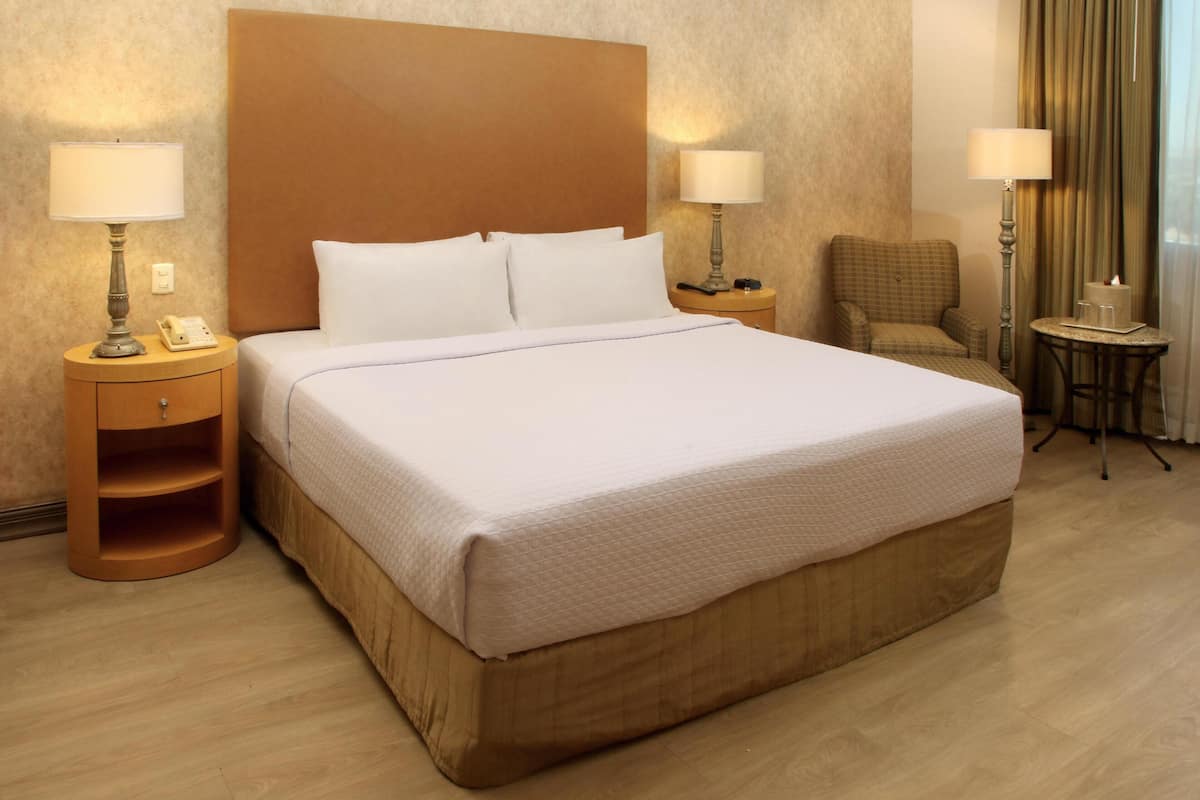 A hotel room with a large bed, two bedside tables with lamps, a chair, and a small table with a candle.