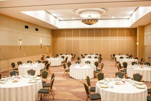 Un salón de banquetes con varias mesas redondas, cada una dispuesta con platos, vasos y cubiertos.