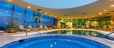 An indoor swimming pool with lounge chairs and potted plants.