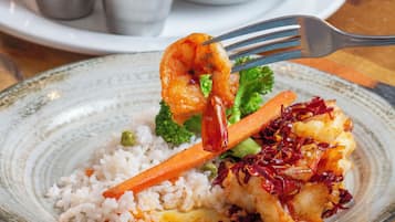 Un plato de comida con arroz, verduras y camarones, acompañado de salsas para mojar y un tazón de comida frita.