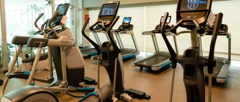 A gym with multiple treadmills and elliptical machines, a digital display showing workout metrics, and a mirror reflecting the equipment.