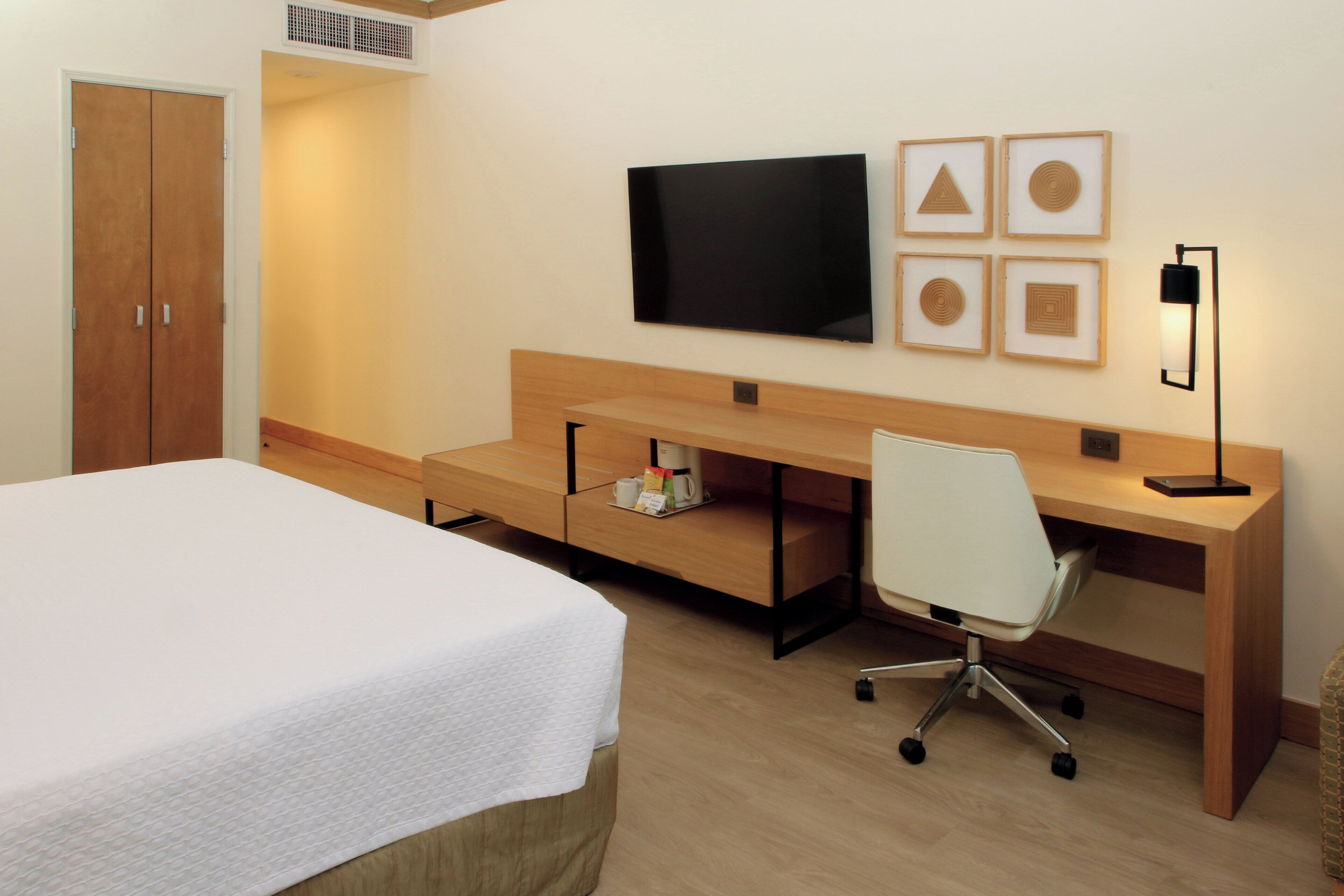 Habitación de hotel con cama, escritorio, silla, televisor y cuadros en la pared.
