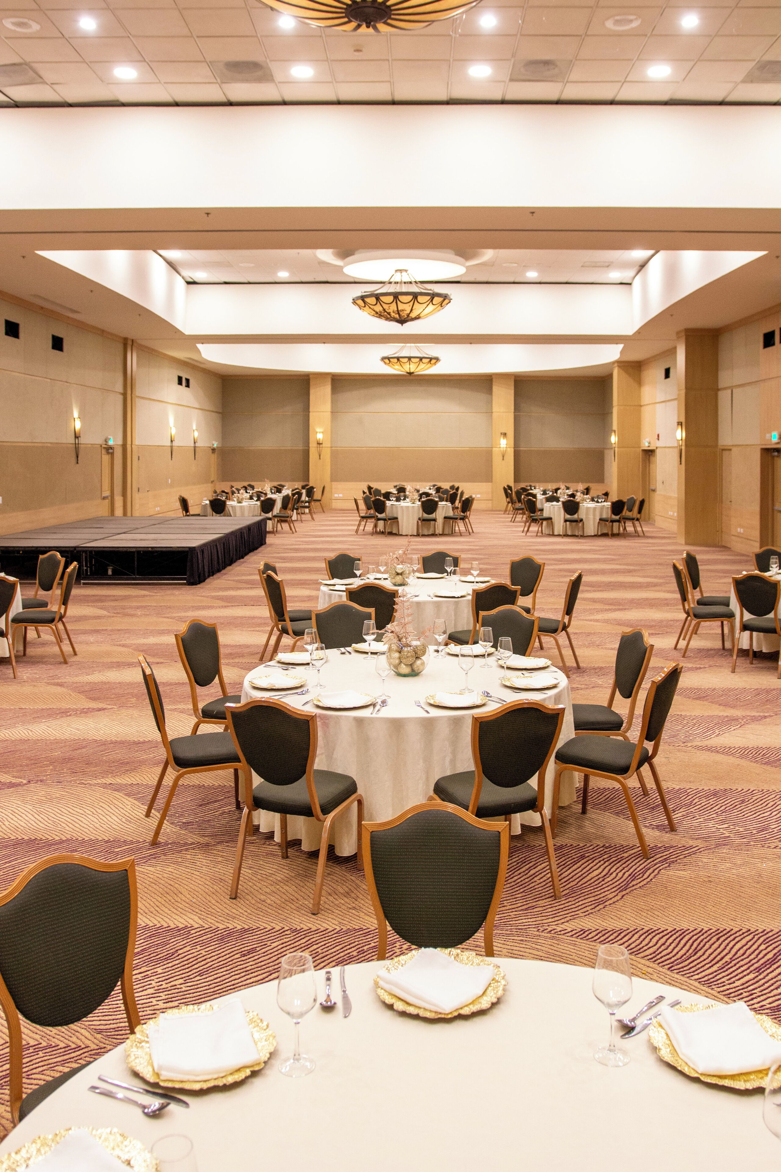 A banquet hall with round tables, chairs, and a stage.