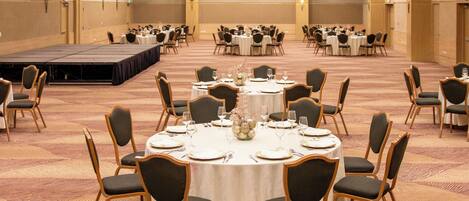 A banquet hall with round tables, chairs, and a stage.