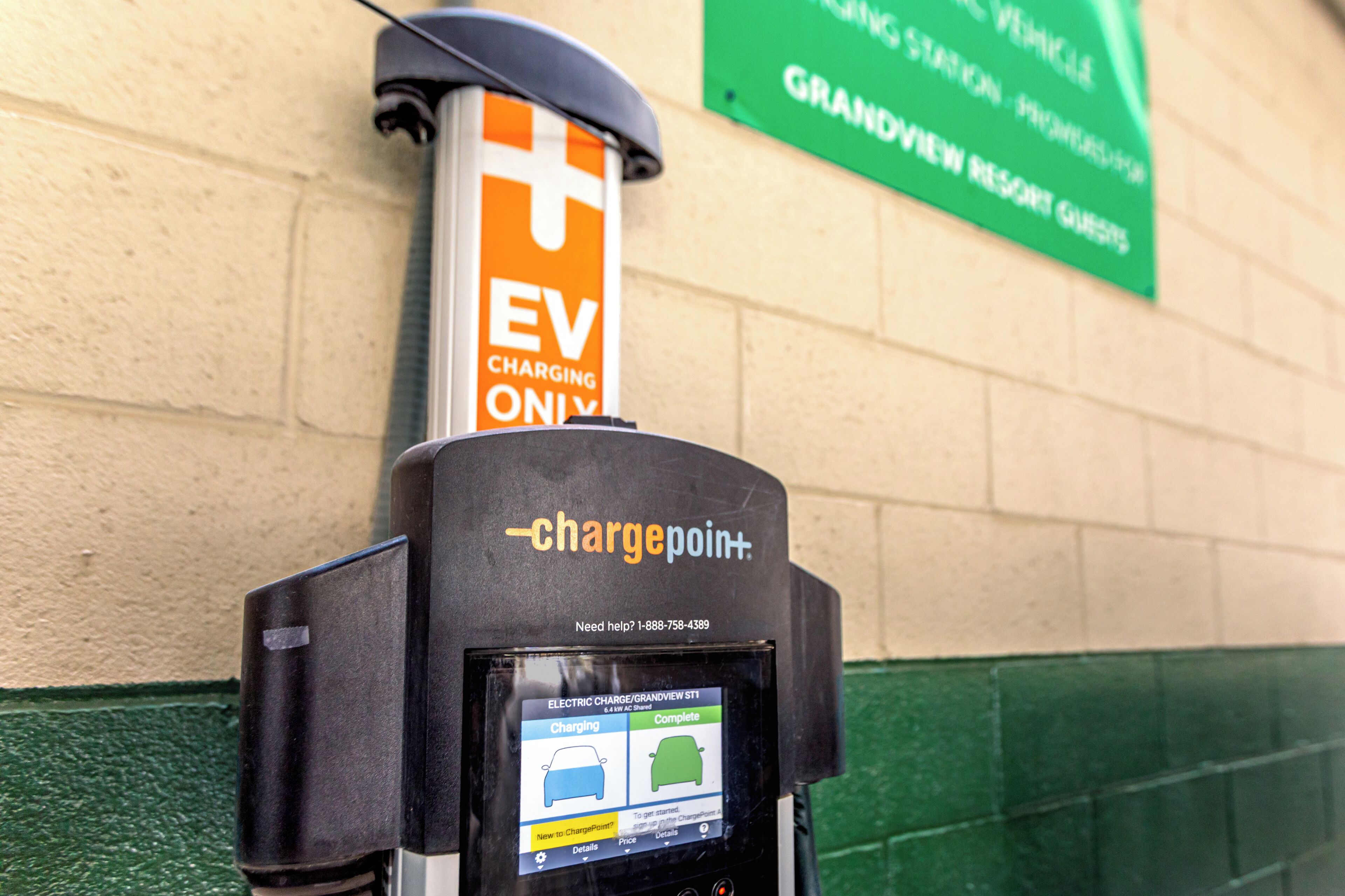 Una estación de carga para vehículos eléctricos, con pantalla digital y un cartel que indica que es solo para vehículos eléctricos, con un letrero verde en el fondo.
