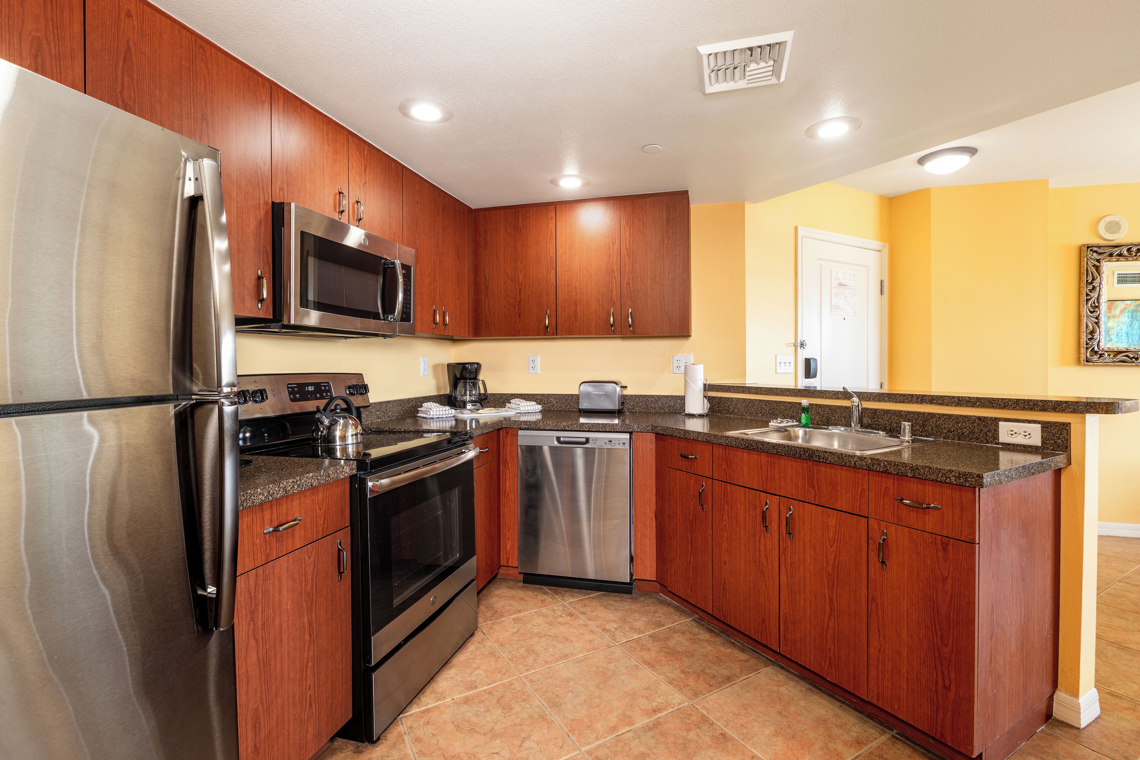 A kitchen with wooden cabinets, stainless steel appliances, and a yellow wall.