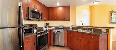 A kitchen with wooden cabinets, stainless steel appliances, and a yellow wall.