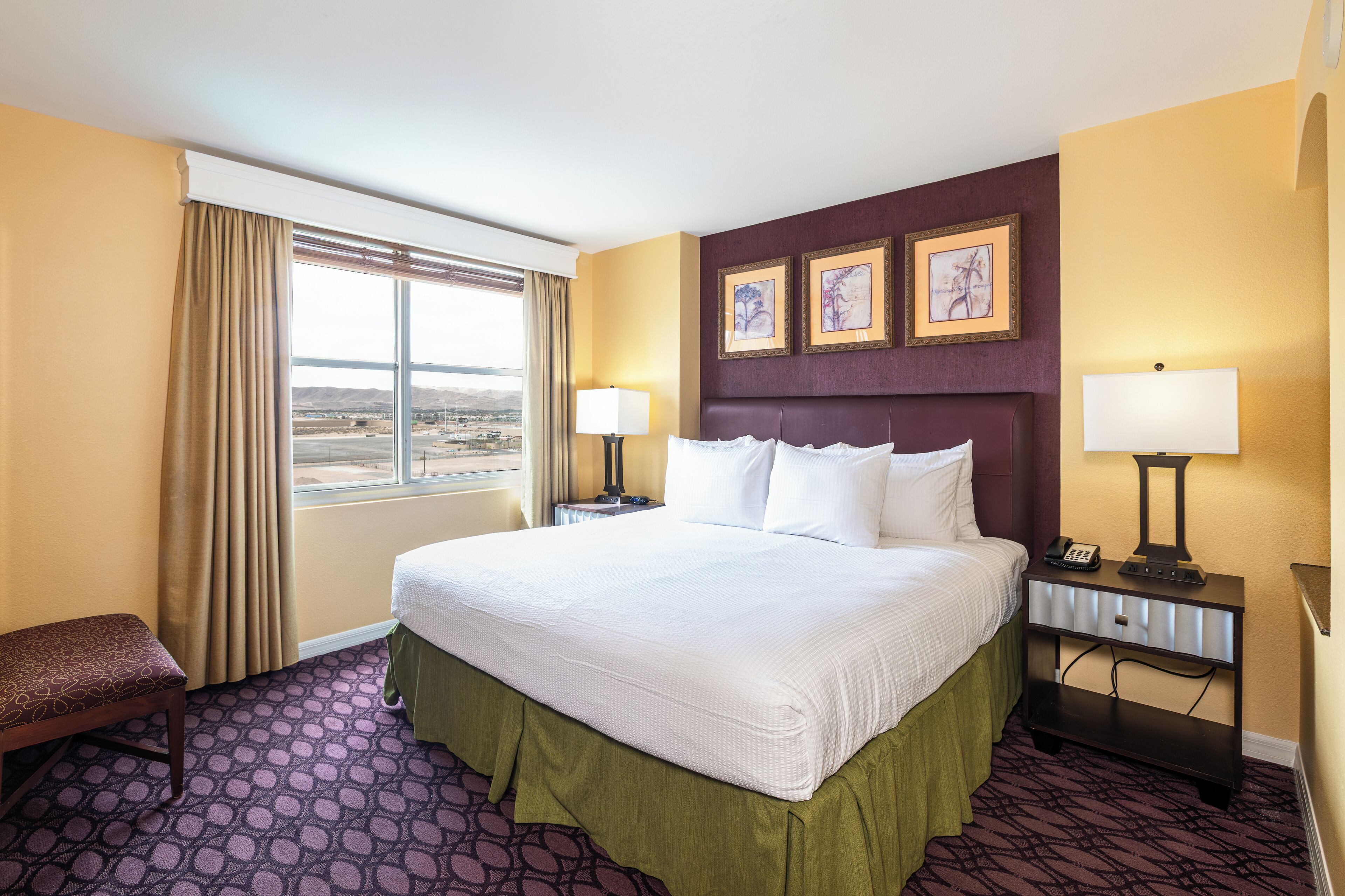 Habitación de hotel con una cama grande, dos mesitas de noche con lámparas, un banco y vistas al paisaje a través de la ventana.