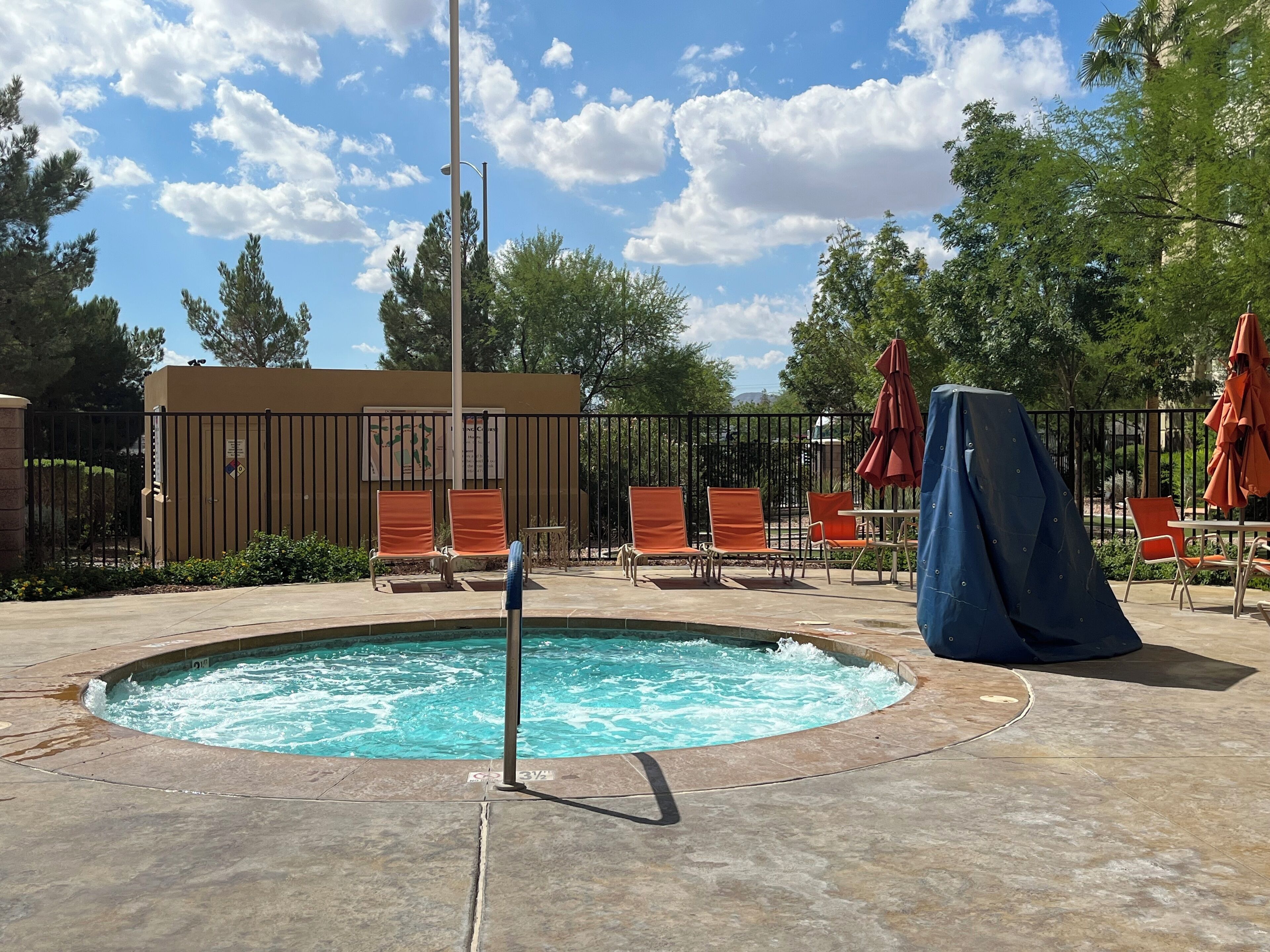 Une piscine entourée d’une clôture et d’arbres, avec des chaises longues et des parasols.