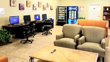 Een computerruimte met meerdere werkplekken, een automaat en een zithoek met een bank en stoelen.
