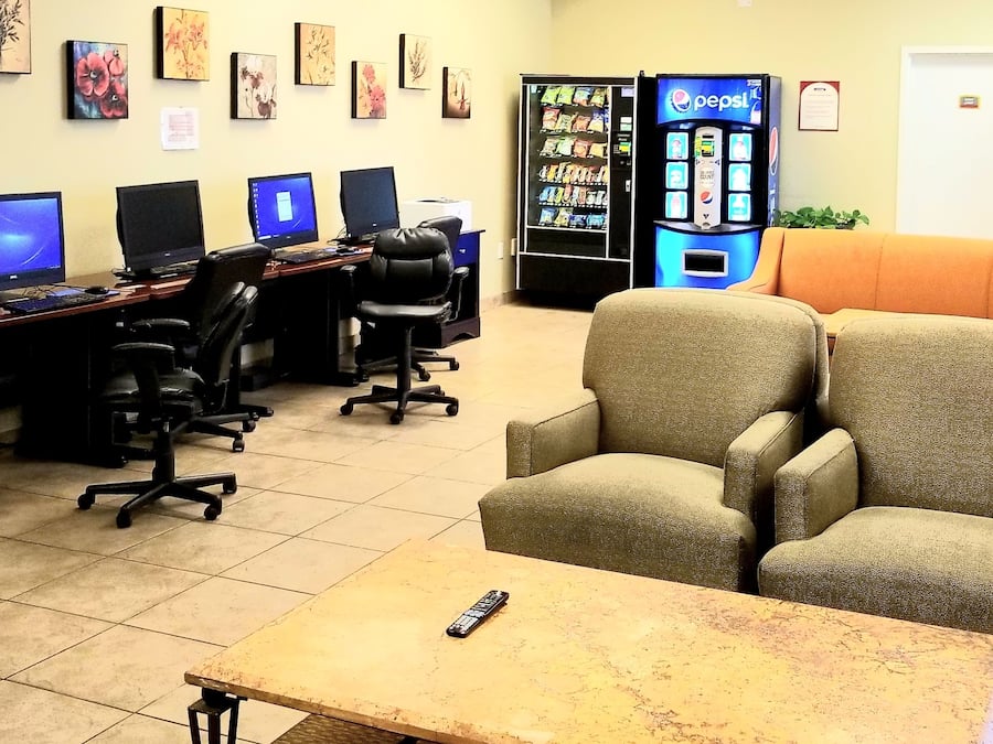 Een computerruimte met meerdere werkplekken, een automaat en een zithoek met een bank en stoelen.