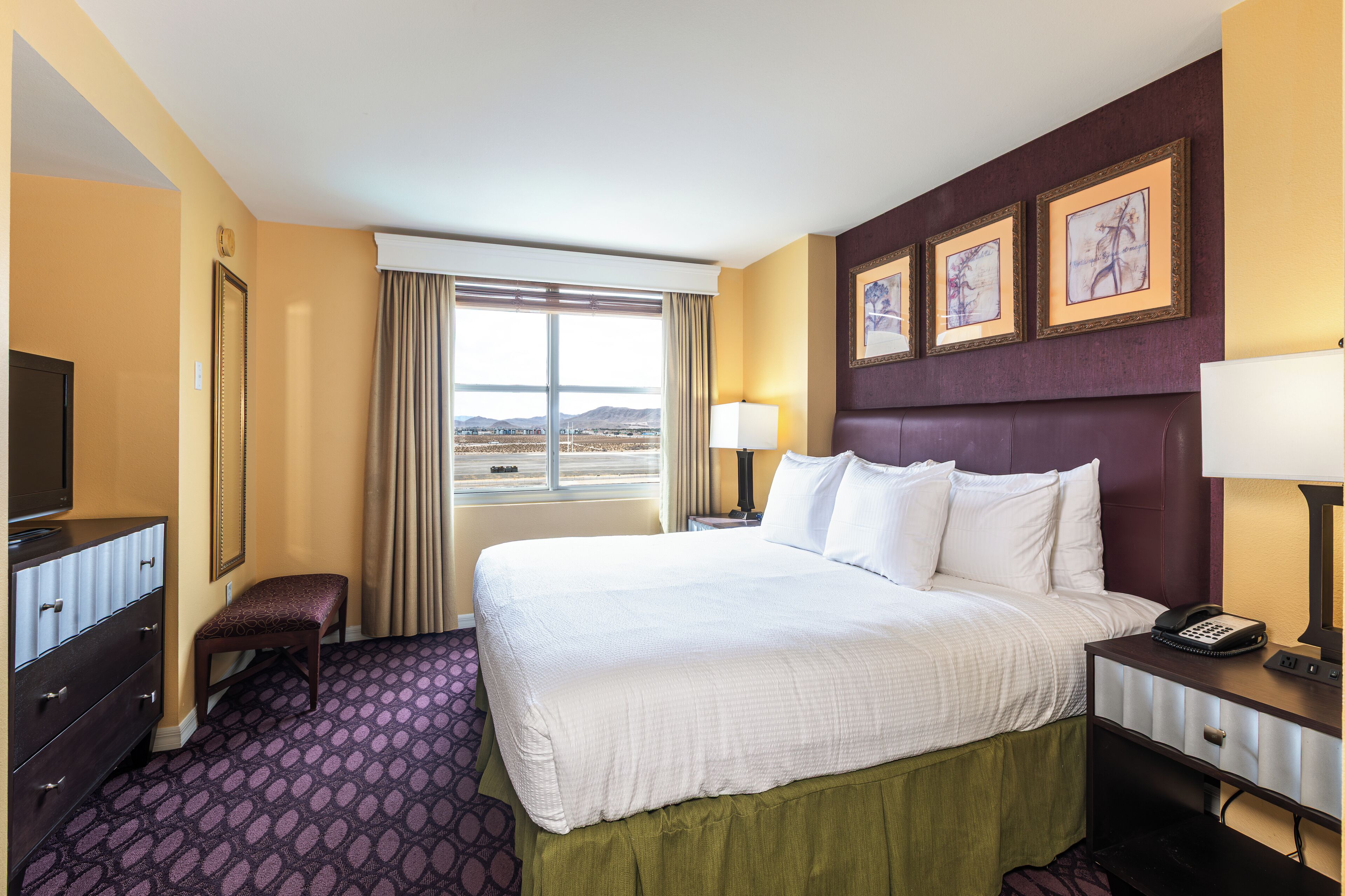 Habitación de hotel con una cama grande, un escritorio con lámpara, teléfono, una silla, cómoda y ventana con vistas a las montañas.