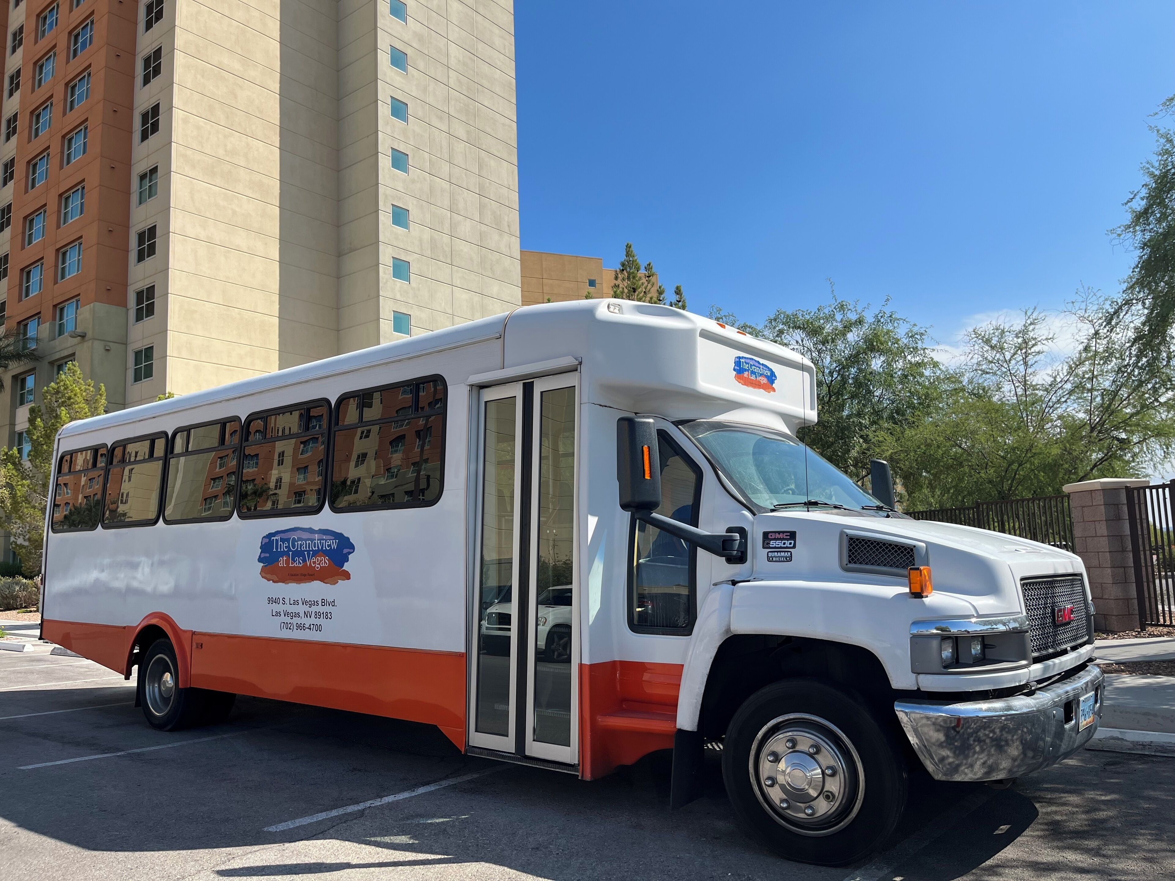 Un autobús blanco y naranja con la marca "The Grandview at Las Vegas" estacionado en un estacionamiento.