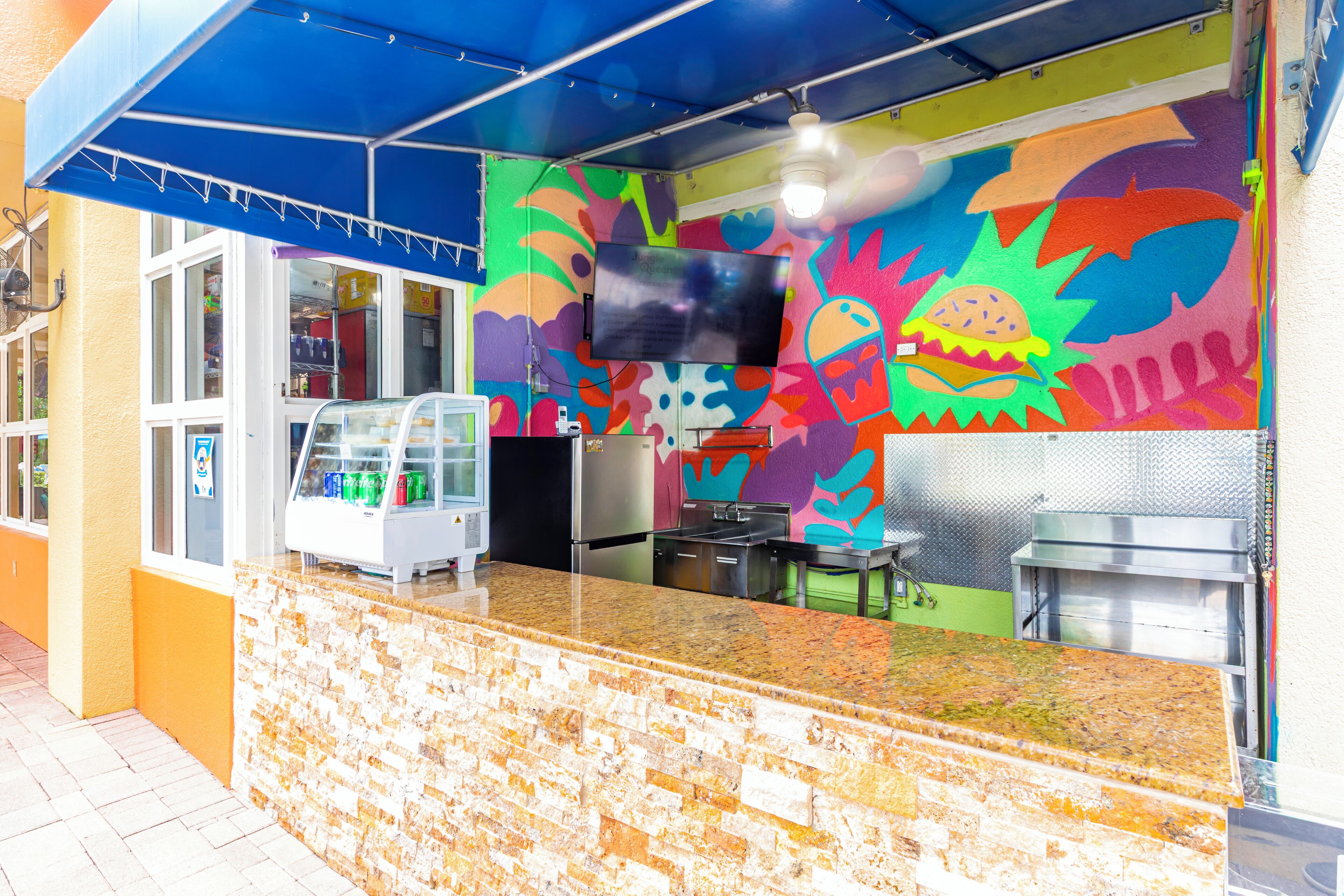 Un quiosco de comida de colores llamativos, con mostrador, una pantalla de televisión y un refrigerador.