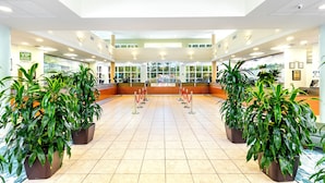 Un hall espacioso con mostrador de recepción, plantas en macetas y suelo de baldosas.