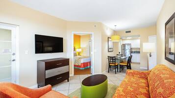 Habitación de hotel con televisor, sofá, mesa de comedor con sillas, zona de cocina y cama con colcha colorida.